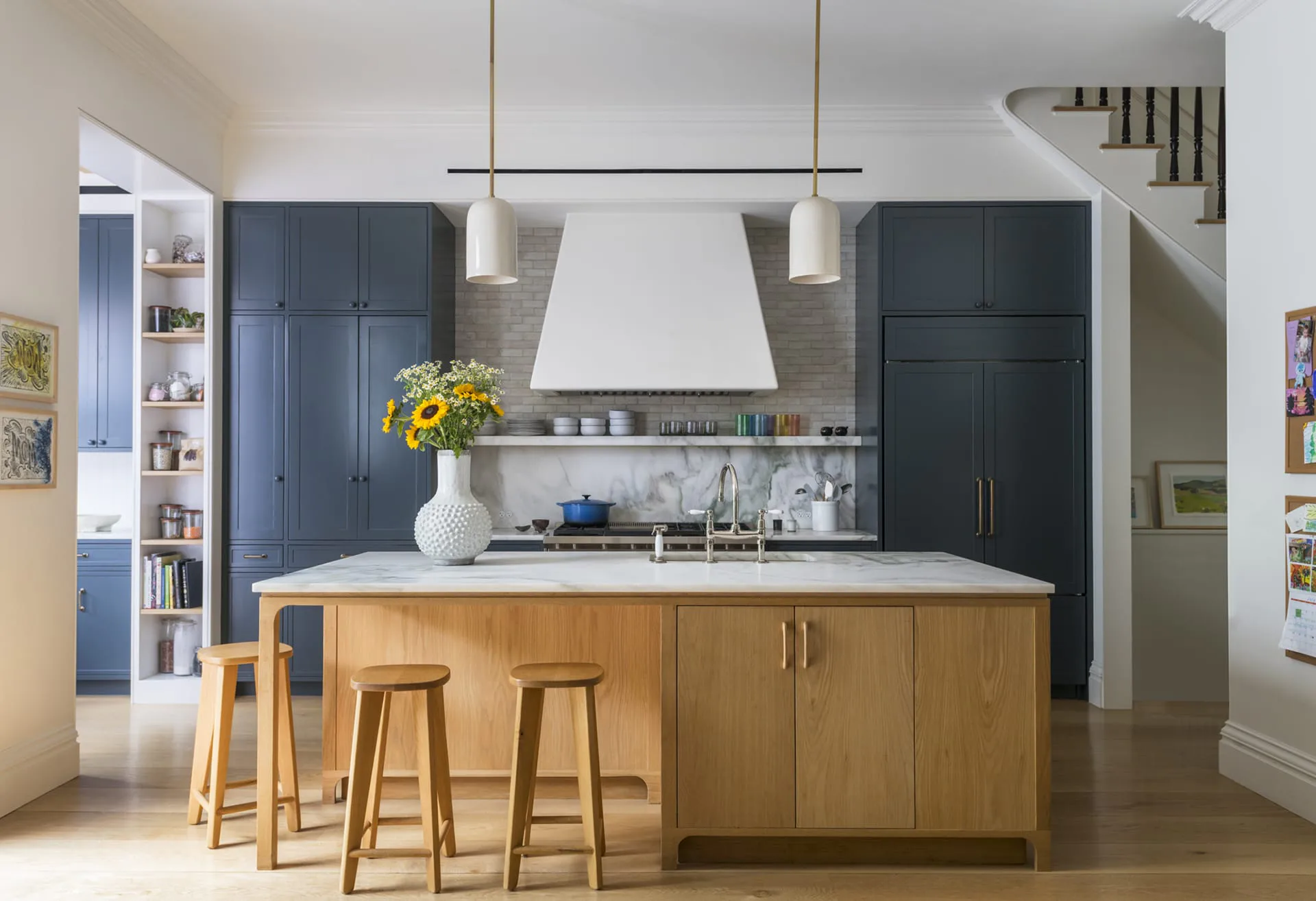 Modern kitchen with natural wood island, dark navy cabinetry, marble backsplash, and pendant lighting designed by Sohui Kim.