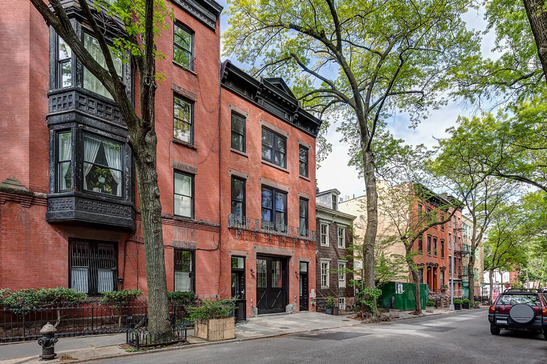 Brick rowhouses with restored facades, large windows, and mature trees lining a quiet urban street by Sohui Kim.