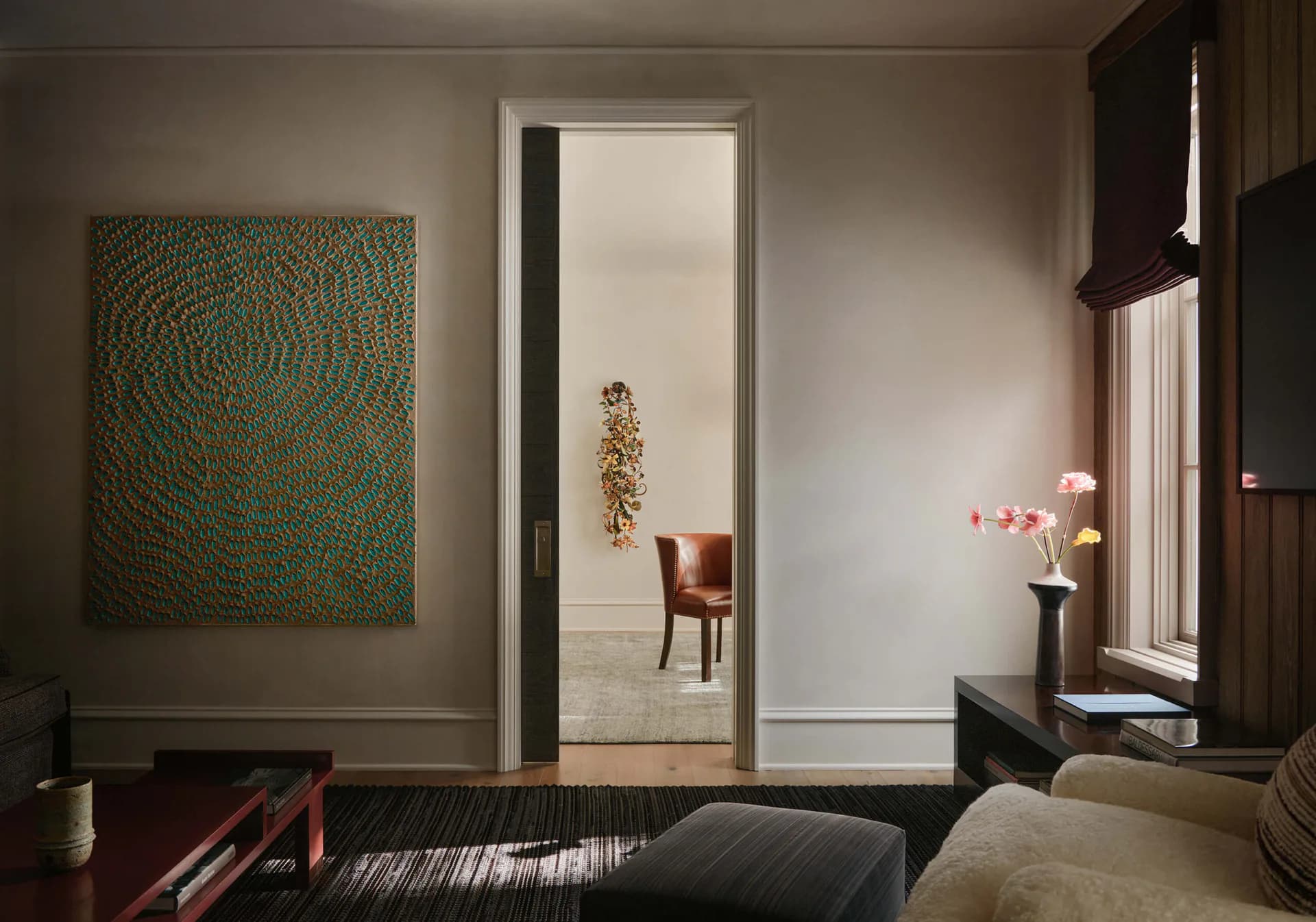 Modern bedroom with dark wood elements, neutral walls, contemporary artwork, and view into adjacent room with chair, designed by Soo Chung.