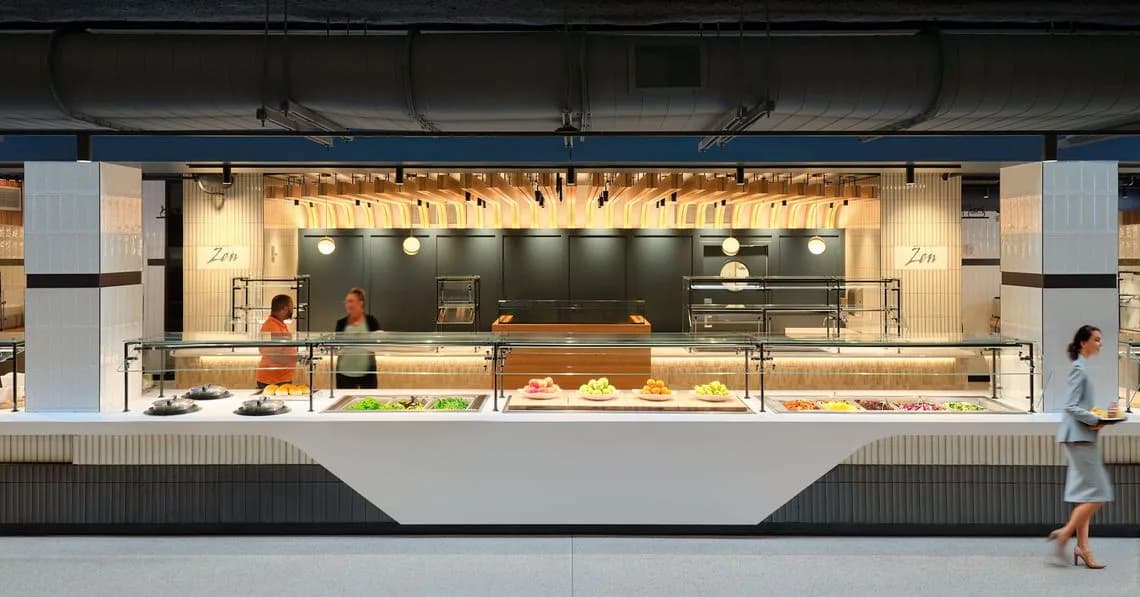 Modern food service counter with clean lines, warm wood accents, and minimalist design featuring a sleek white facade and backlit shelving by Sophia Le.