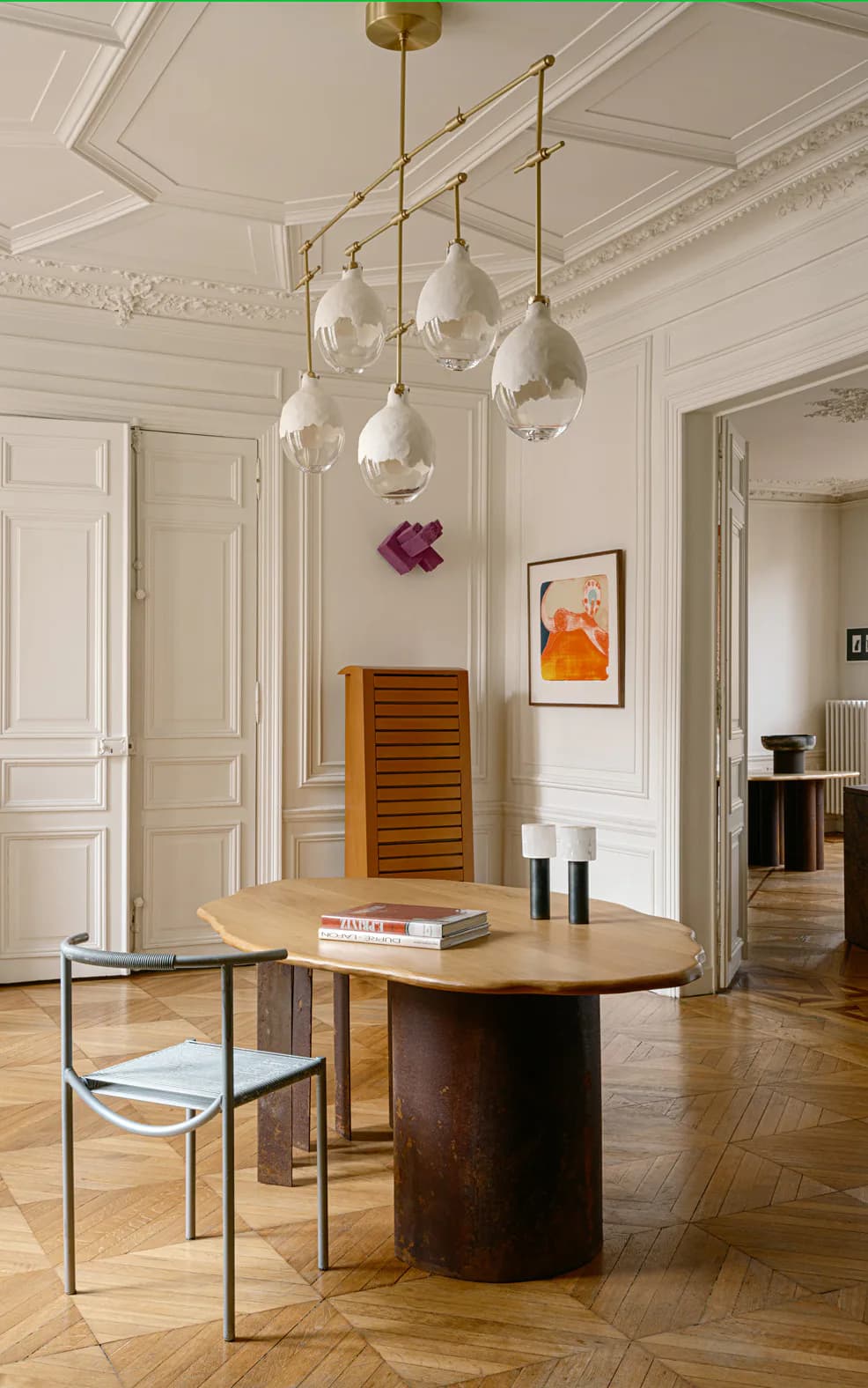 Cream-toned Parisian apartment with oval wood dining table, brass pendant lights, and neoclassical moldings by Sophie Dries.