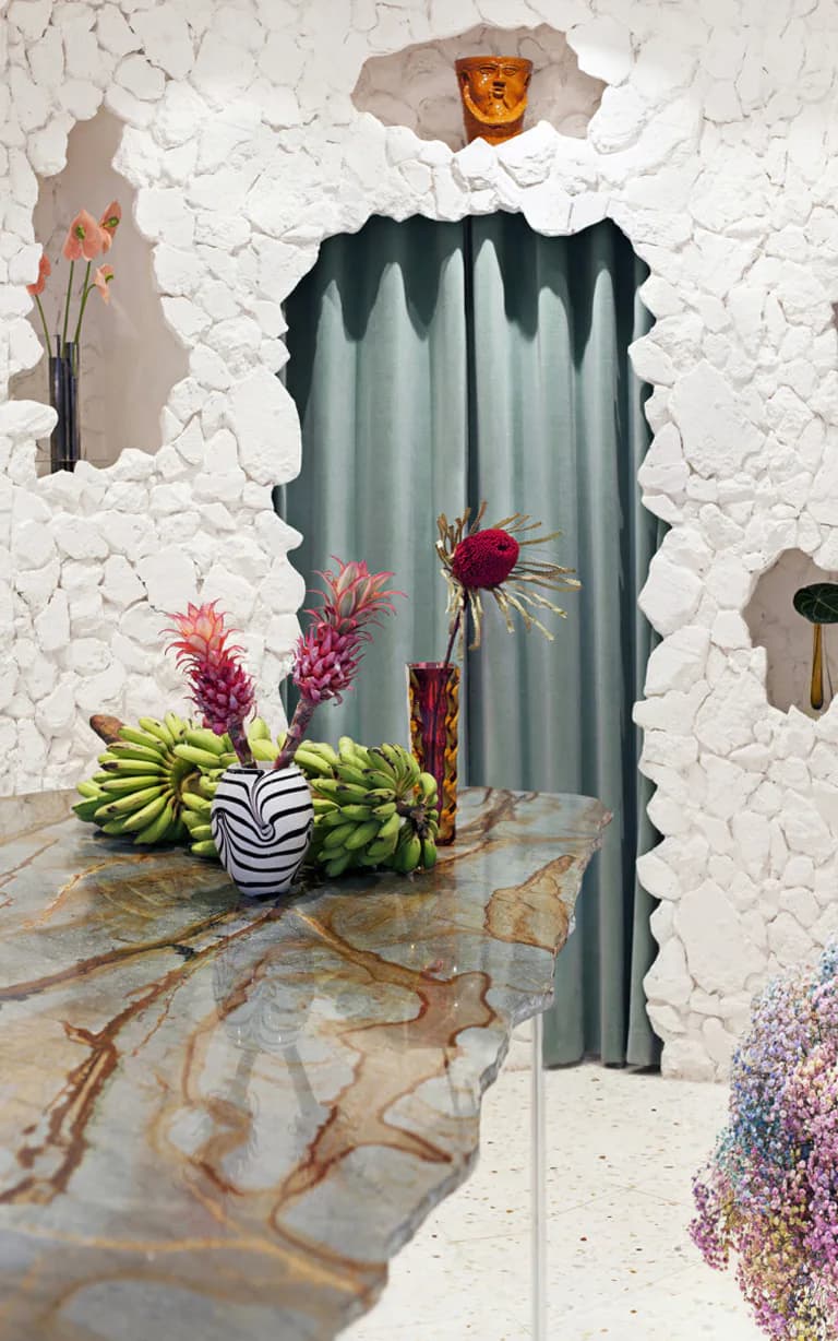 White textured wall with arched doorway opening to gray curtains, styled with tropical fruits and pink protea flowers in zebra vase by Sophie Dries.