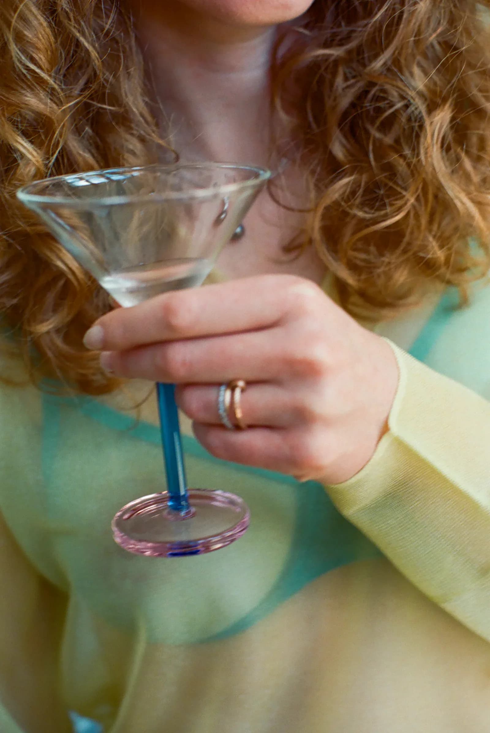 A hand holding a colorful martini glass with a blue stem and pink base, showcasing glassware design by Sophie Lou Jacobsen.