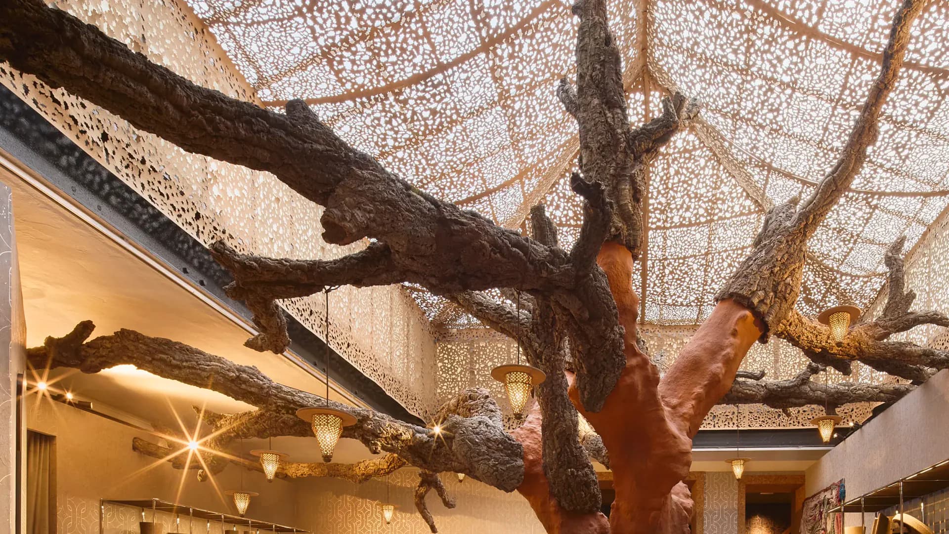 Modern interior with dramatic gnarled tree branch installation suspended from geometric mesh ceiling, warm ambient lighting, minimalist gallery space by Stephan Ritzer.