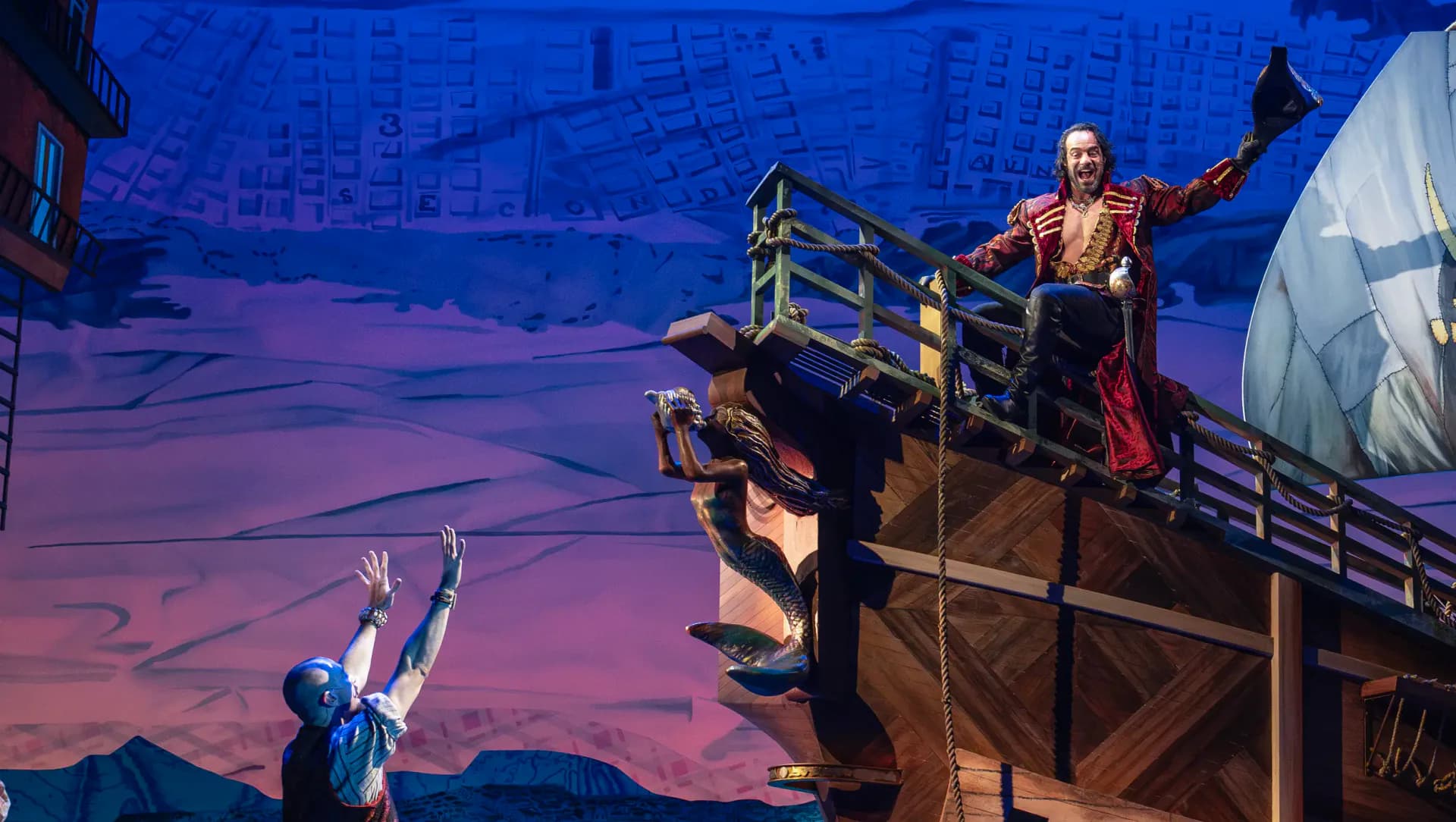 A theatrical stage set featuring a wooden ship structure with dramatic purple and blue lighting, designed by Stephan Ritzer.