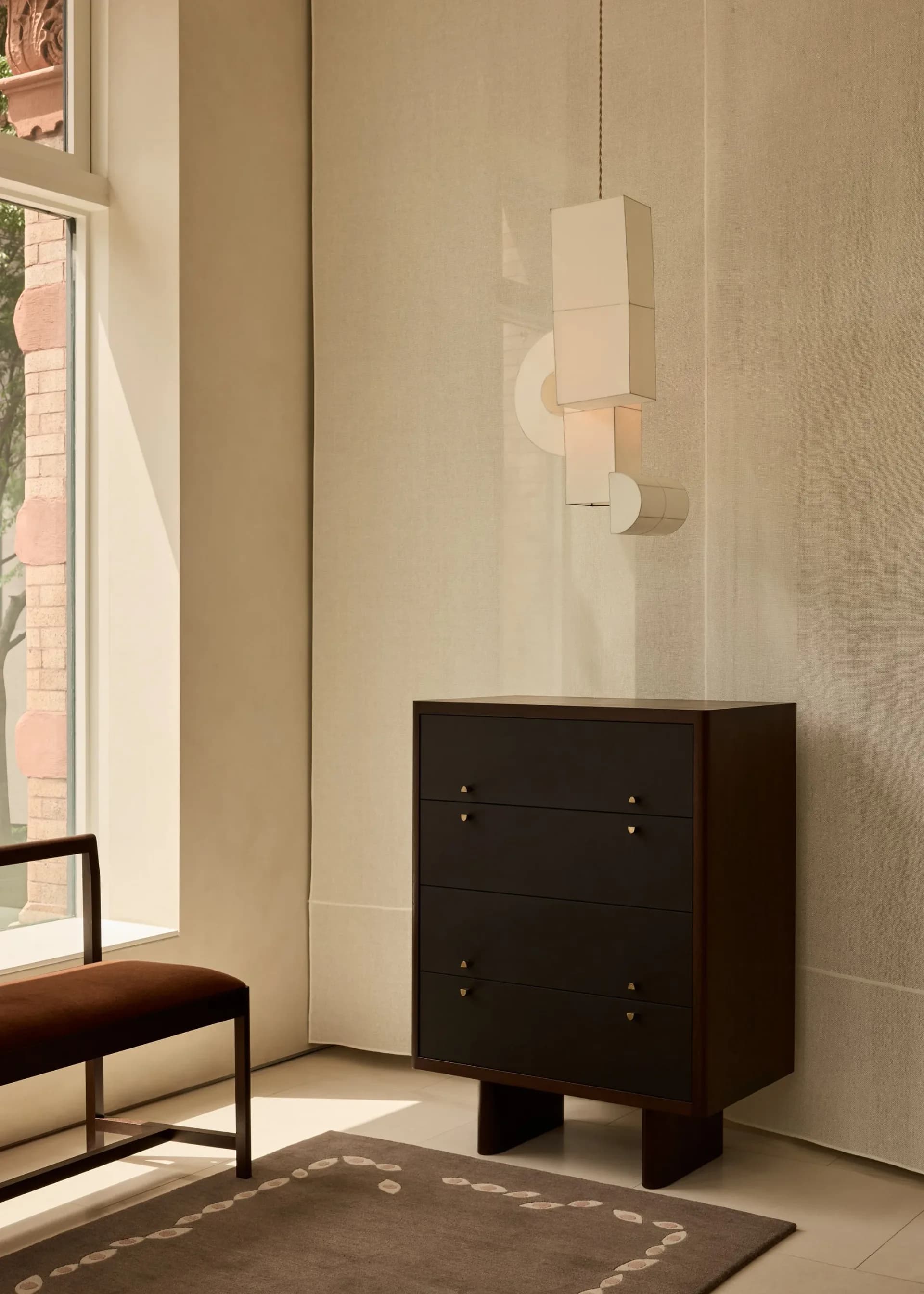 Minimalist interior with dark wooden dresser, cream walls, pendant lighting, and geometric rug by Stephanie Beamer.