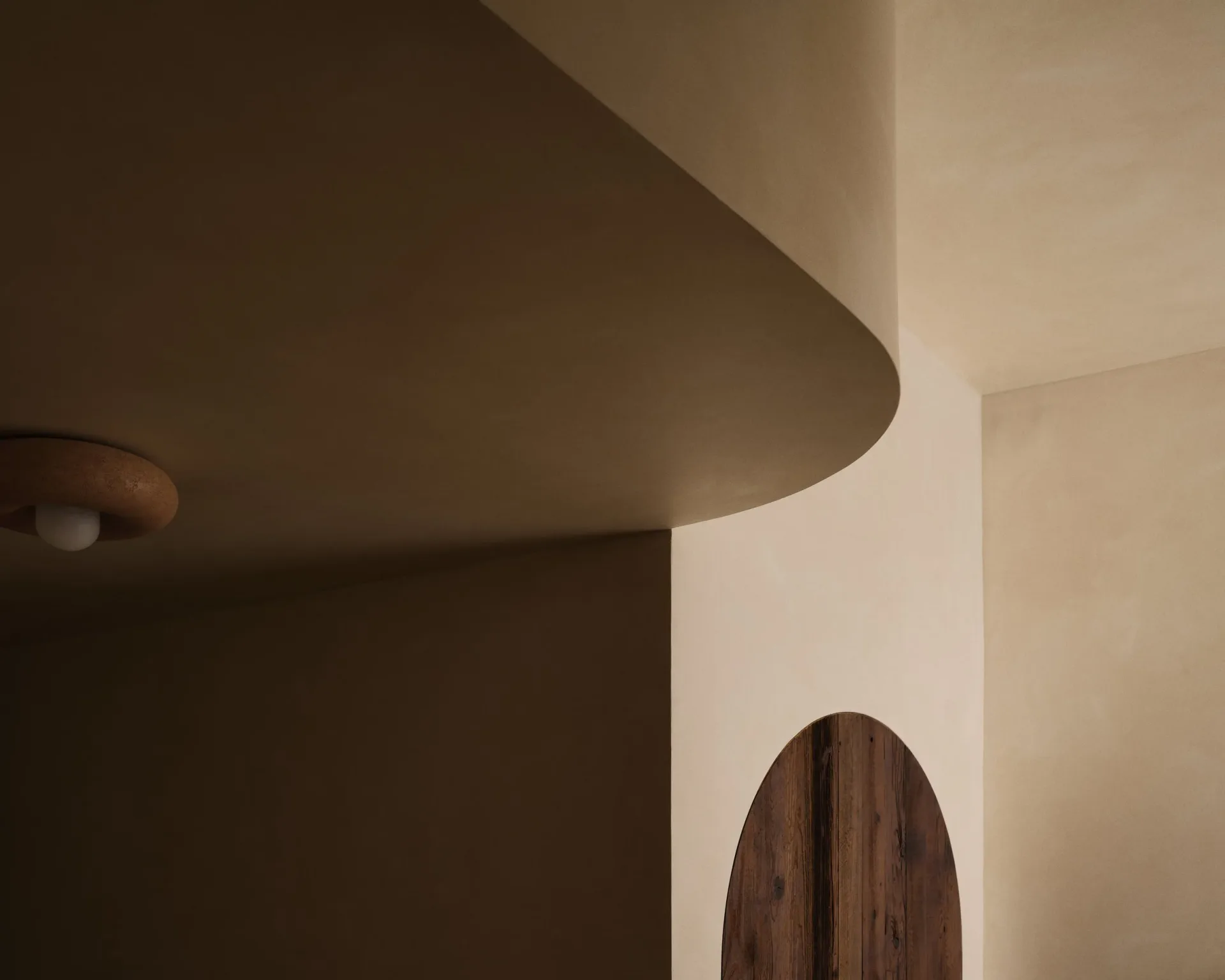 Curved ceiling detail in warm neutral tones with curved wooden element below, showcasing sculptural architectural design by Stephanie Betesh.