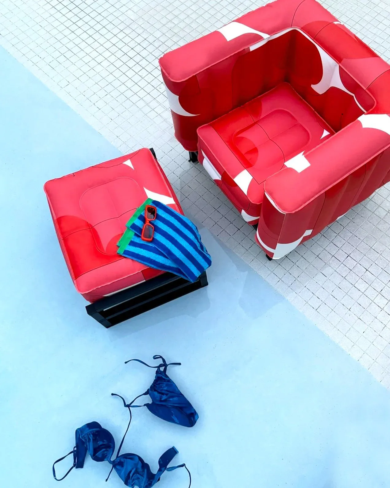 Overhead view of red upholstered lounge seating with geometric white patterns and blue kite-shaped fabric elements arranged by a pool, designed by Stephanie Eventov.