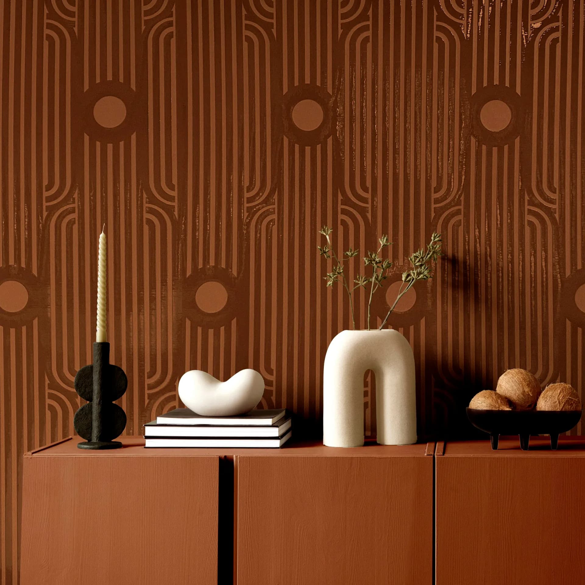 Warm terracotta interior with vertically ribbed wallpaper featuring geometric patterns, styled credenza displaying ceramic vessels, candlestick, books, and decorative objects by Stephanie Eventov.