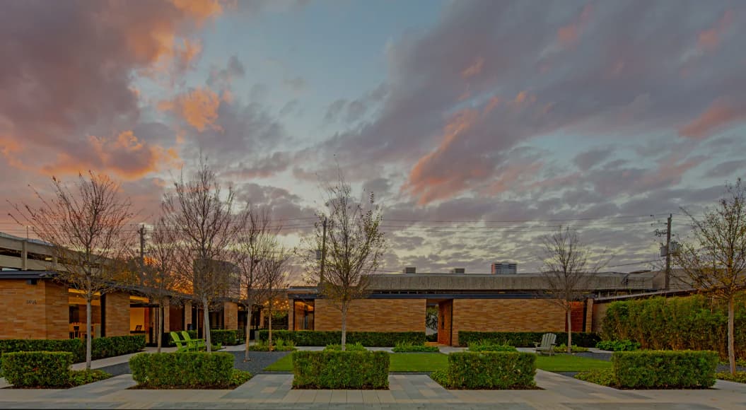 Modern brick institutional building with warm evening sky, bare trees, and manicured hedges, designed by Stephanie Gibson-Roberts.