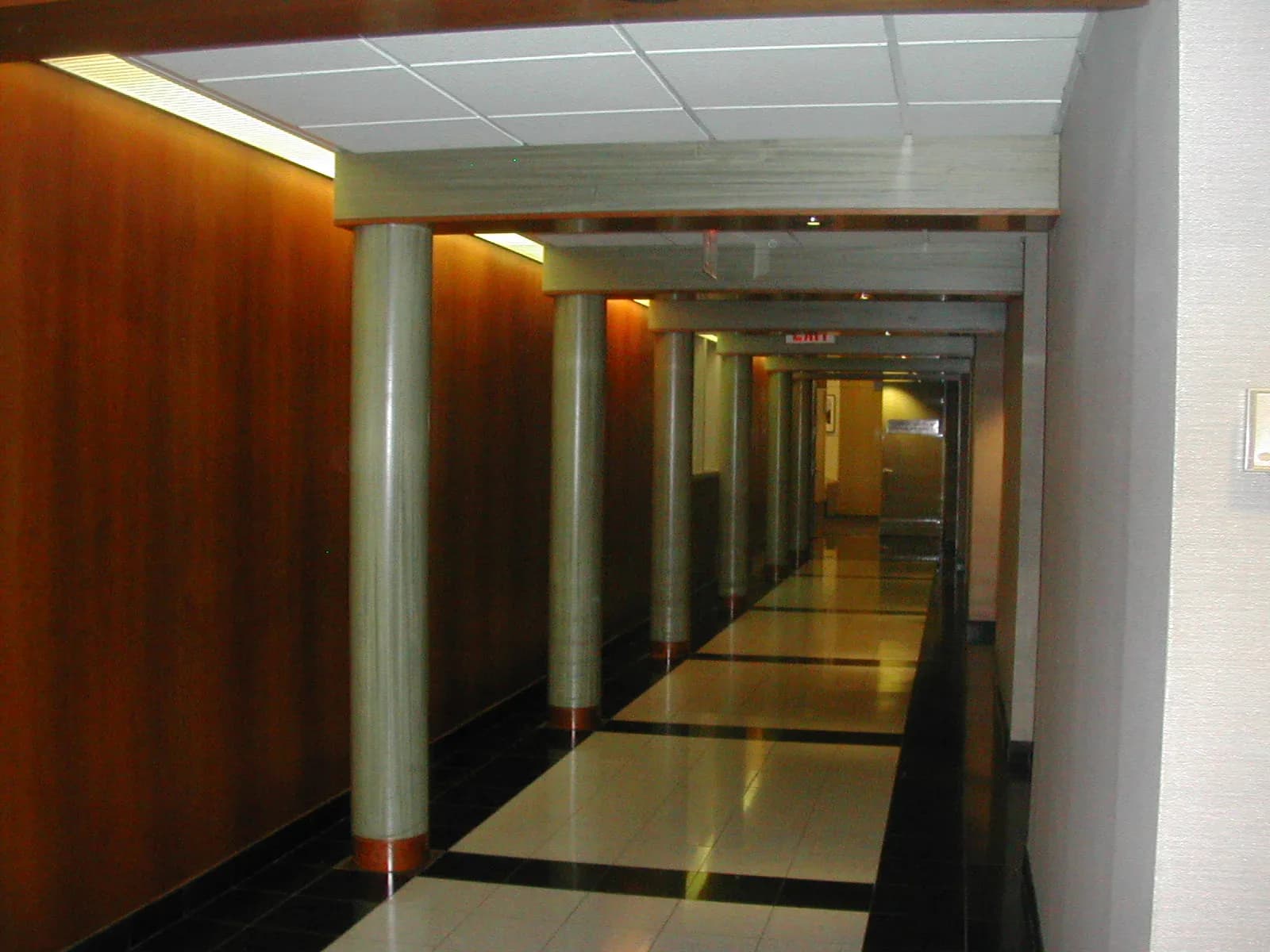 Modern corridor with warm wood paneling, polished concrete flooring, and cylindrical columns; contemporary hallway interior by Stephanie Lichtenstein.