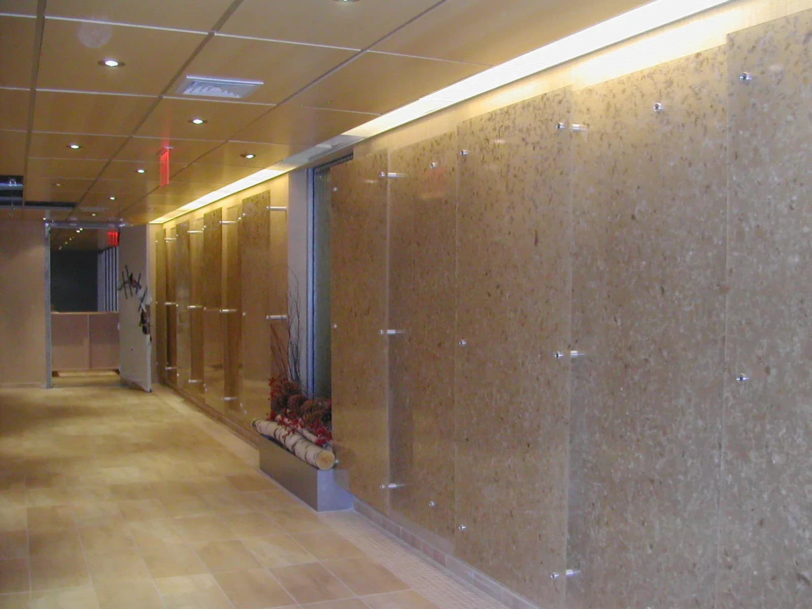 Modern corridor with glass-fronted display cases, warm ambient lighting, stone accent wall, and polished flooring by Stephanie Lichtenstein.