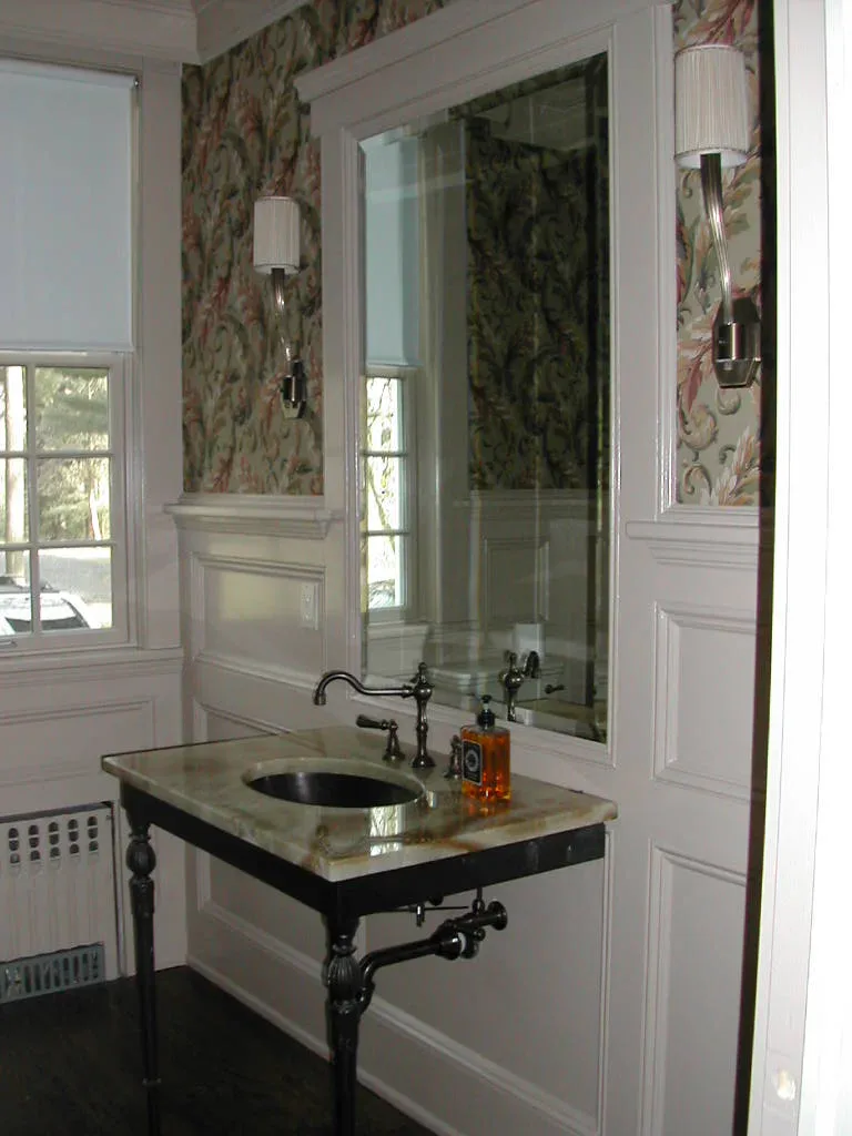 Elegant bathroom vanity with marble countertop, black metal frame basin, and large framed mirror against floral wallpapered walls by Stephanie Lichtenstein.