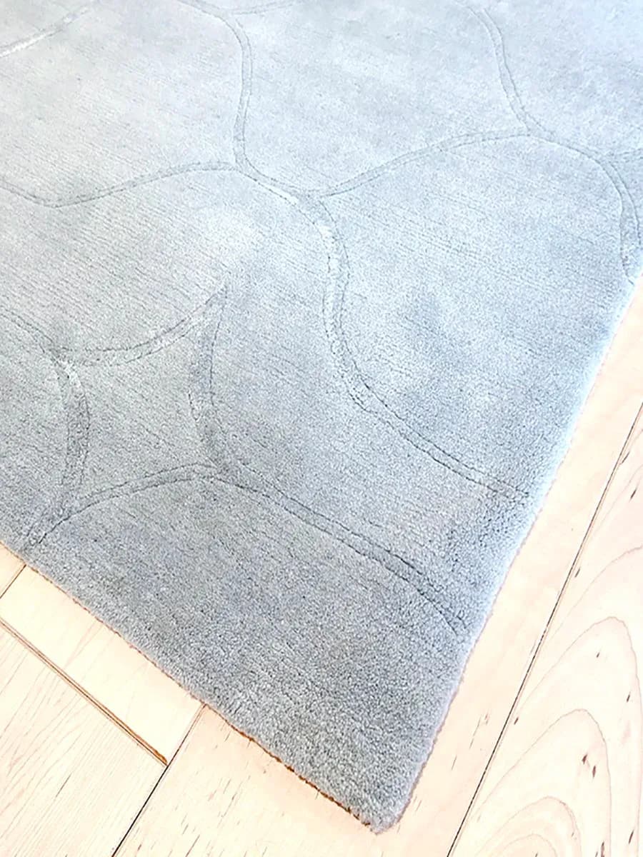 Gray wool area rug with geometric quilted pattern and stitched detailing on light wood flooring by Stephanie Odegard.
