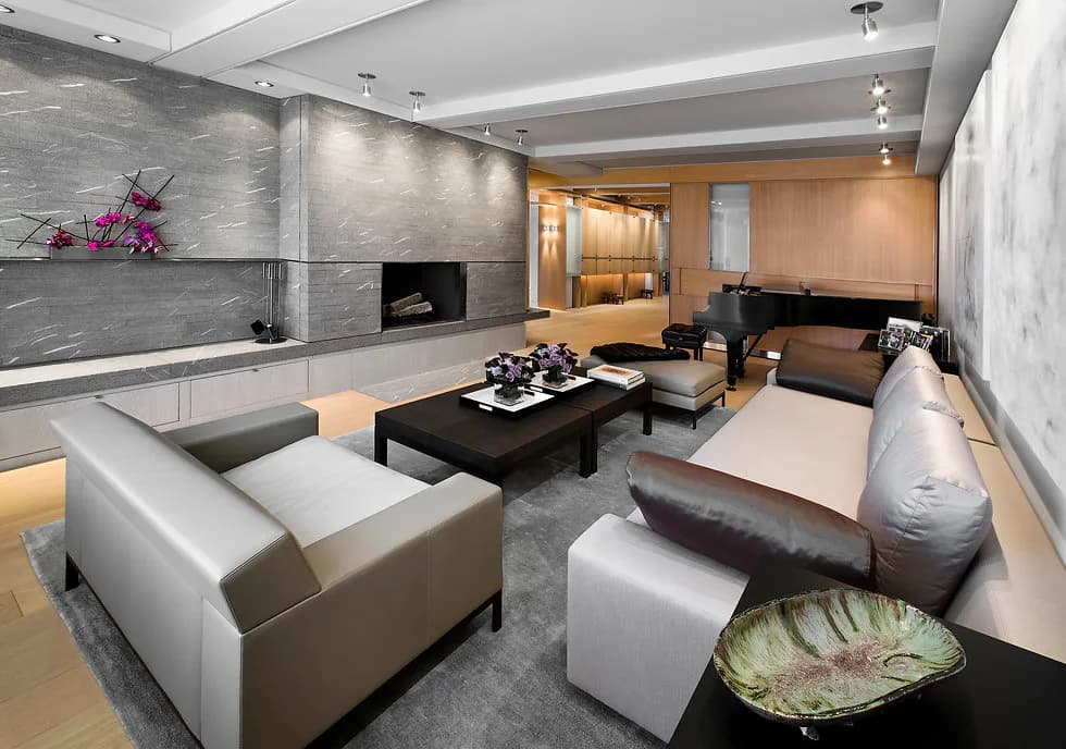 Modern living room with gray stone fireplace, white sofas, black coffee table, and warm wood accents, designed by Stephen Lee.