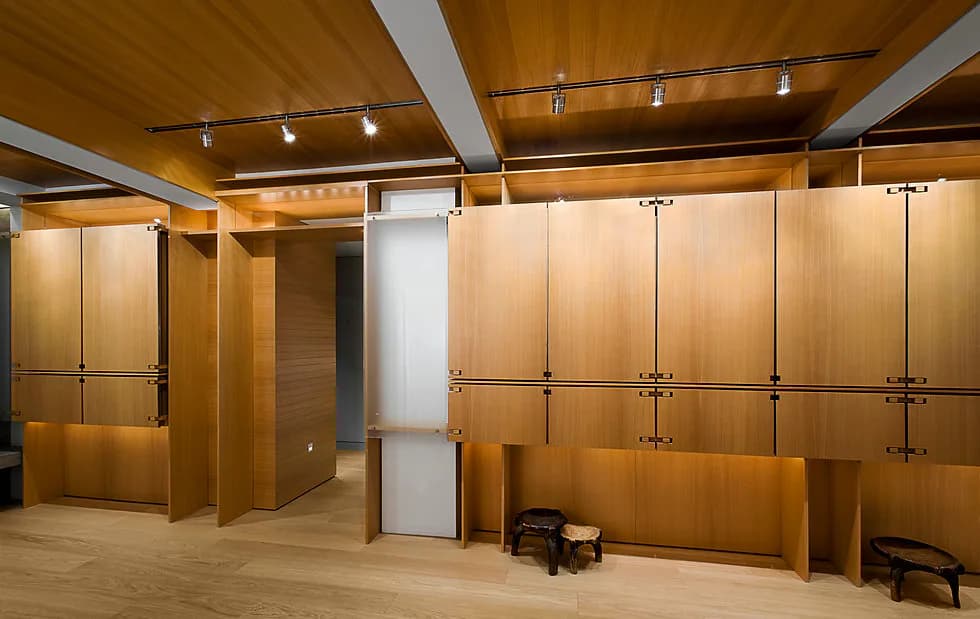 Modern interior showroom with warm wood cabinetry, white columns, track lighting, and polished concrete flooring by Stephen Lee.