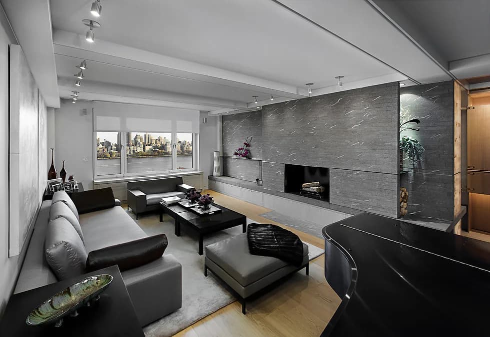 Modern living room with gray upholstered seating, black coffee table, stone fireplace accent wall, and natural wood flooring by Stephen Lee.