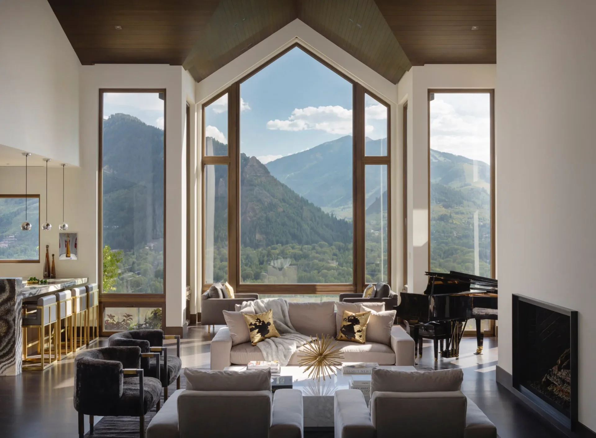 Modern luxury living room with floor-to-ceiling windows framing mountain vistas, featuring gray seating, black grand piano, and geometric architectural ceiling by Sterling McDavid.