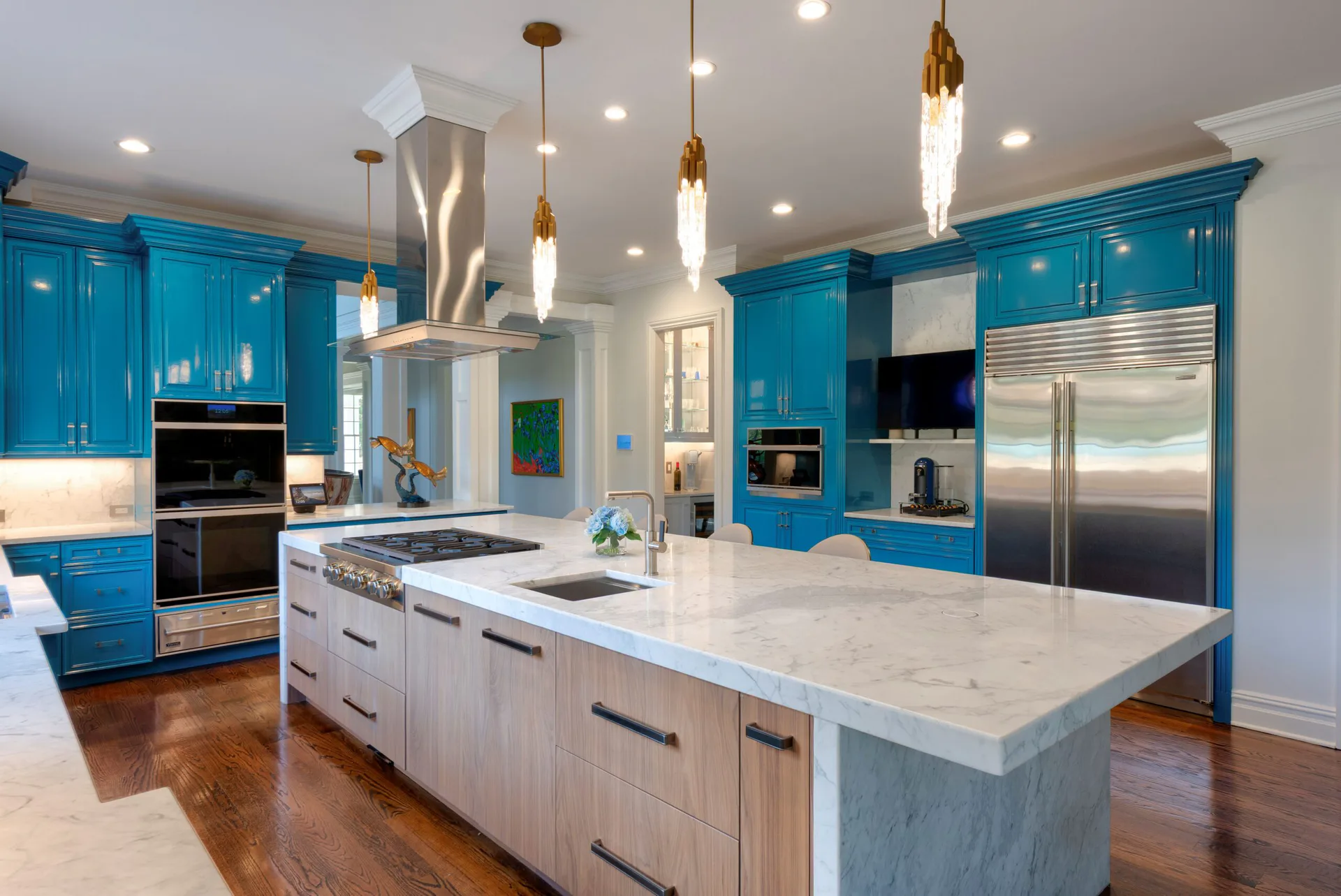 Contemporary kitchen with vibrant turquoise cabinetry, white marble island, stainless steel appliances, and gold pendant lighting by Steve Moran.