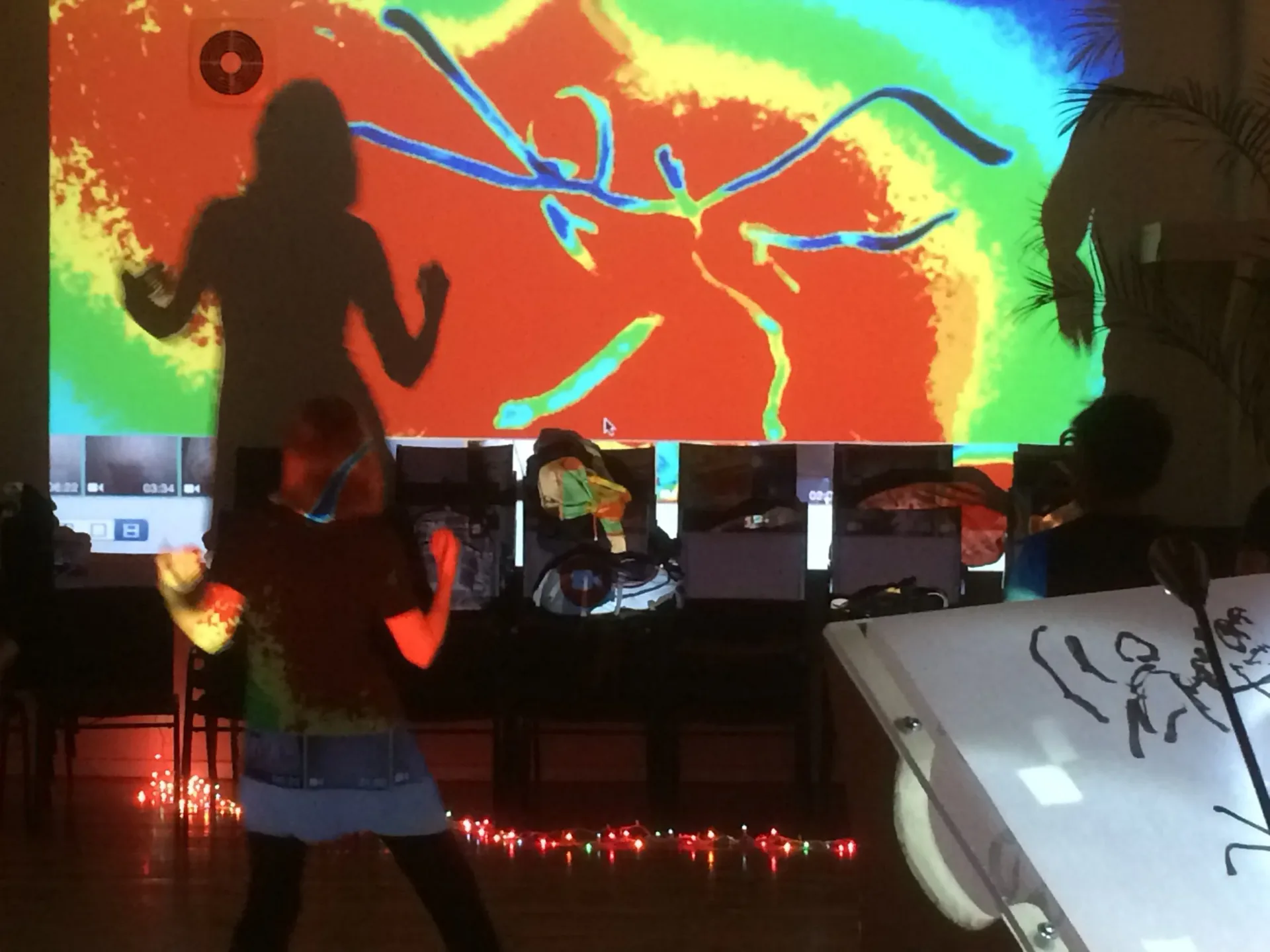 Interactive digital installation with vibrant thermal-imaging projection and silhouetted figures engaging with the display, designed by Stewart Hoyt.