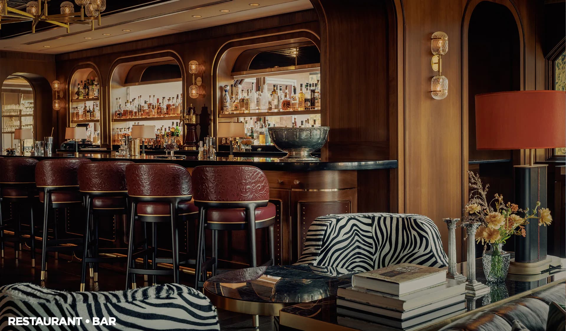 Luxe bar and lounge interior featuring curved wood paneling, mirrored bar back, leather seating, zebra-print accents, and warm ambient lighting by Su Ergeneli.