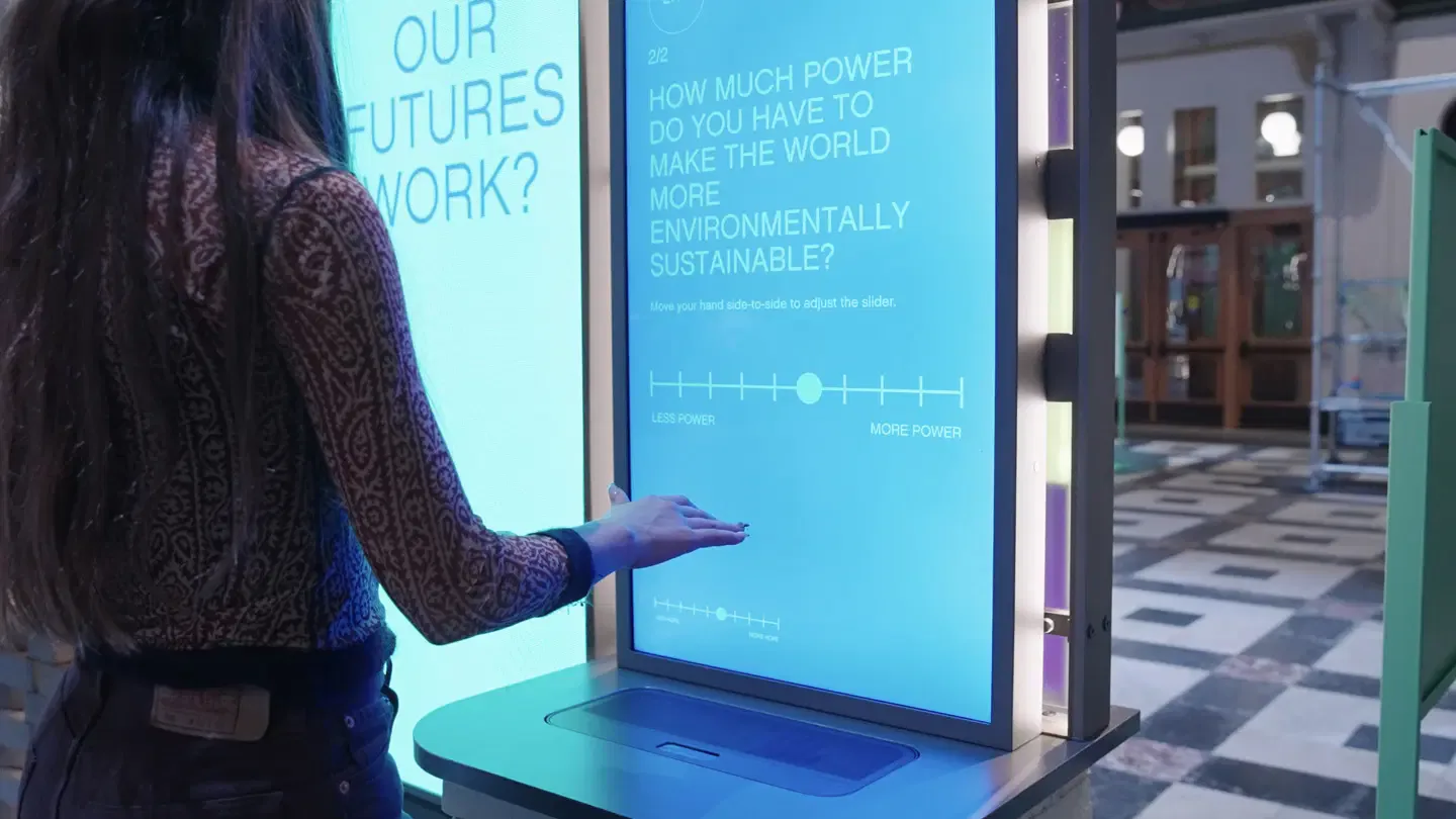 Interactive blue touchscreen display installation with sustainability messaging, mounted in modern corridor with polished flooring, designed by Sunmi Lee.