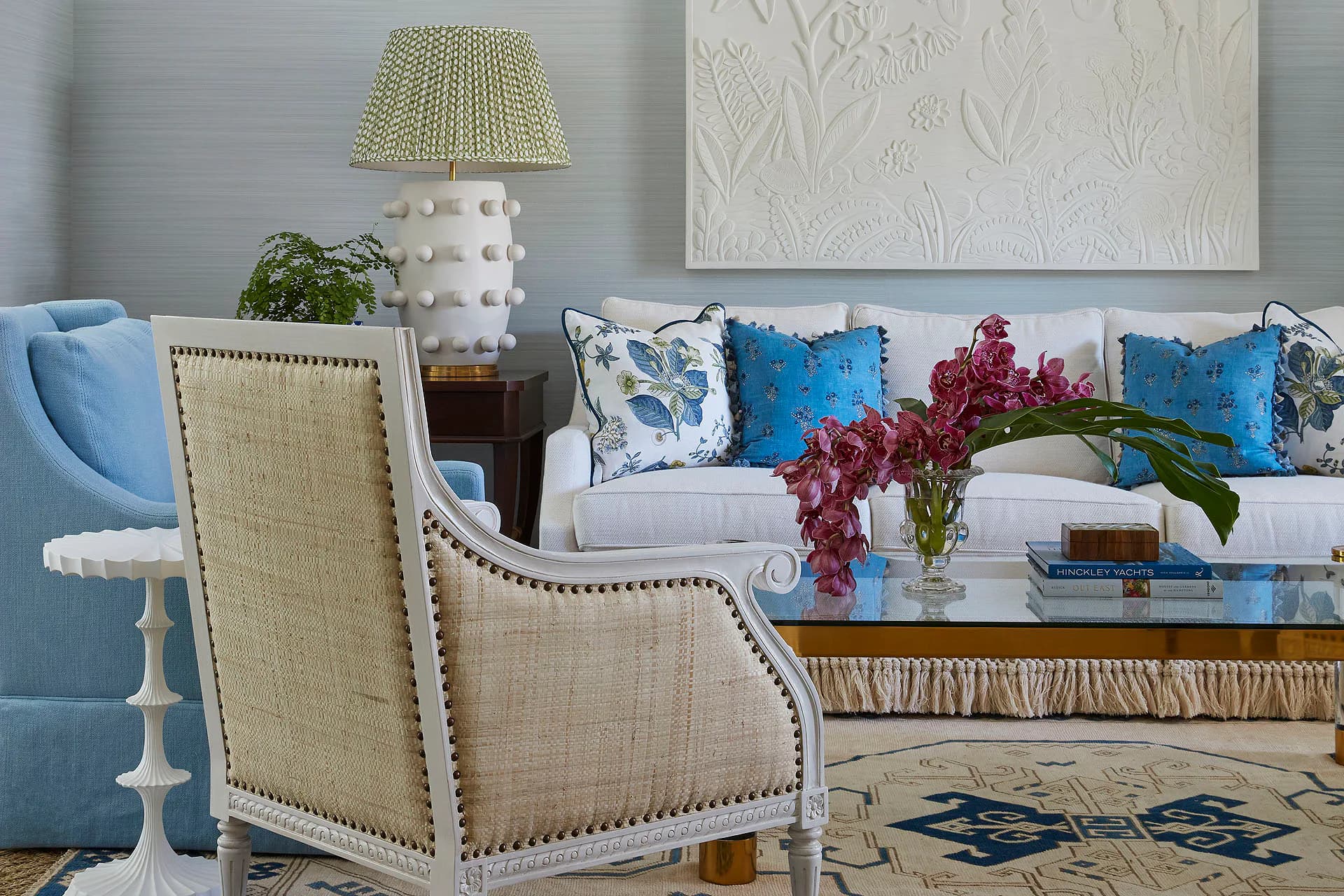 Bright living room with cream upholstered armchair, blue sofa with patterned pillows, brass lamp, and geometric area rug by Susan Carlson.