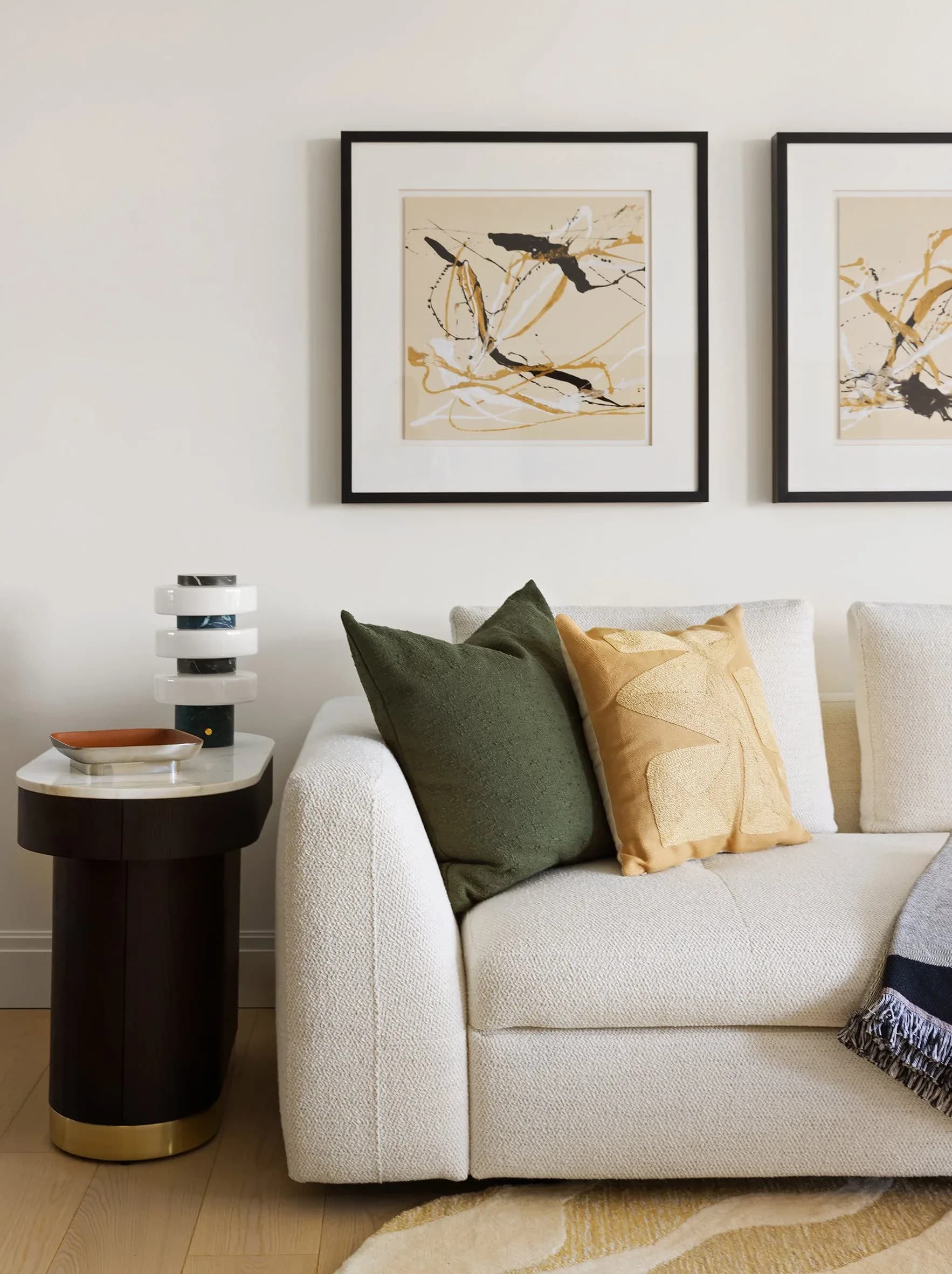 Contemporary living room with cream curved sofa, olive and gold pillows, black side table, and framed bird artwork above by Susan Hughes.