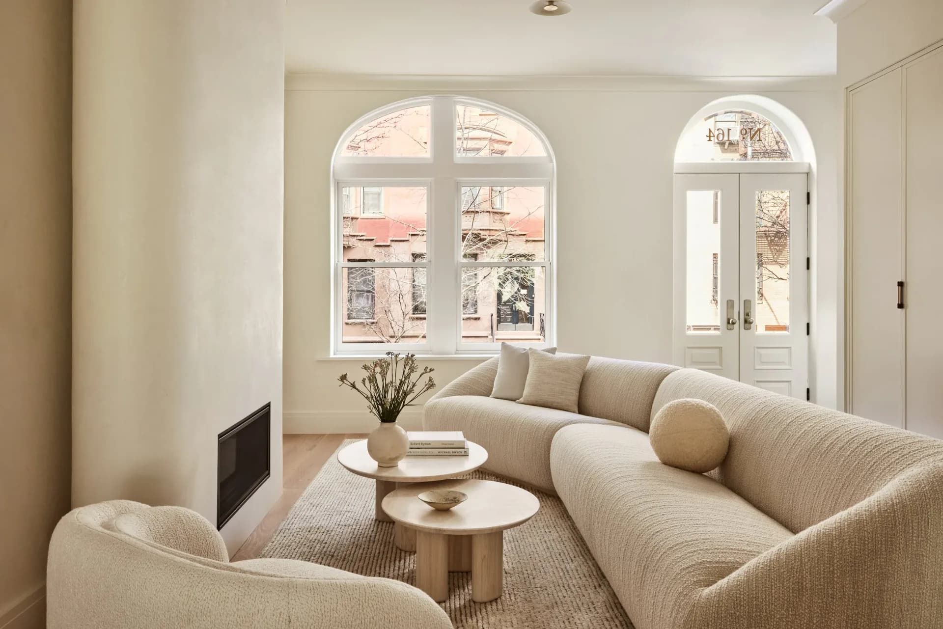 Minimalist living room with curved cream upholstered seating, round wooden tables, arched windows, and neutral palette by Susana Simonpietri.