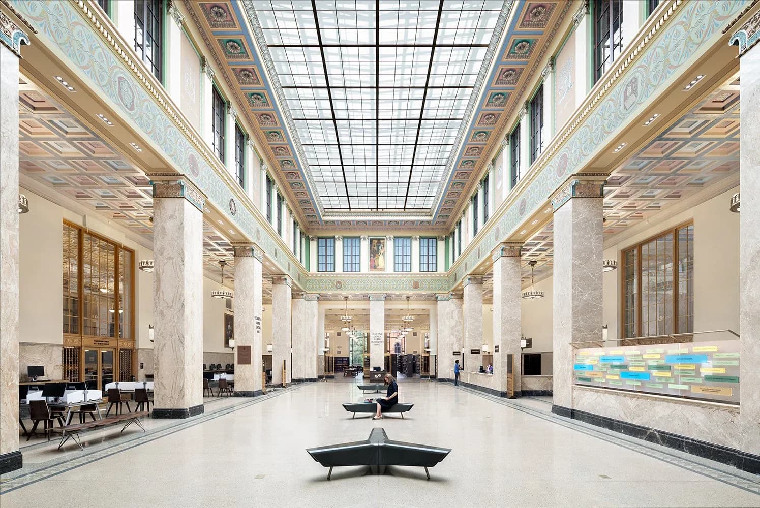 A symmetrical, light-filled corridor with coffered ceilings, classical columns, and centered seating by Suzan Tillotson, displaying characteristics of architectural visualization with idealized proportions and pristine conditions.