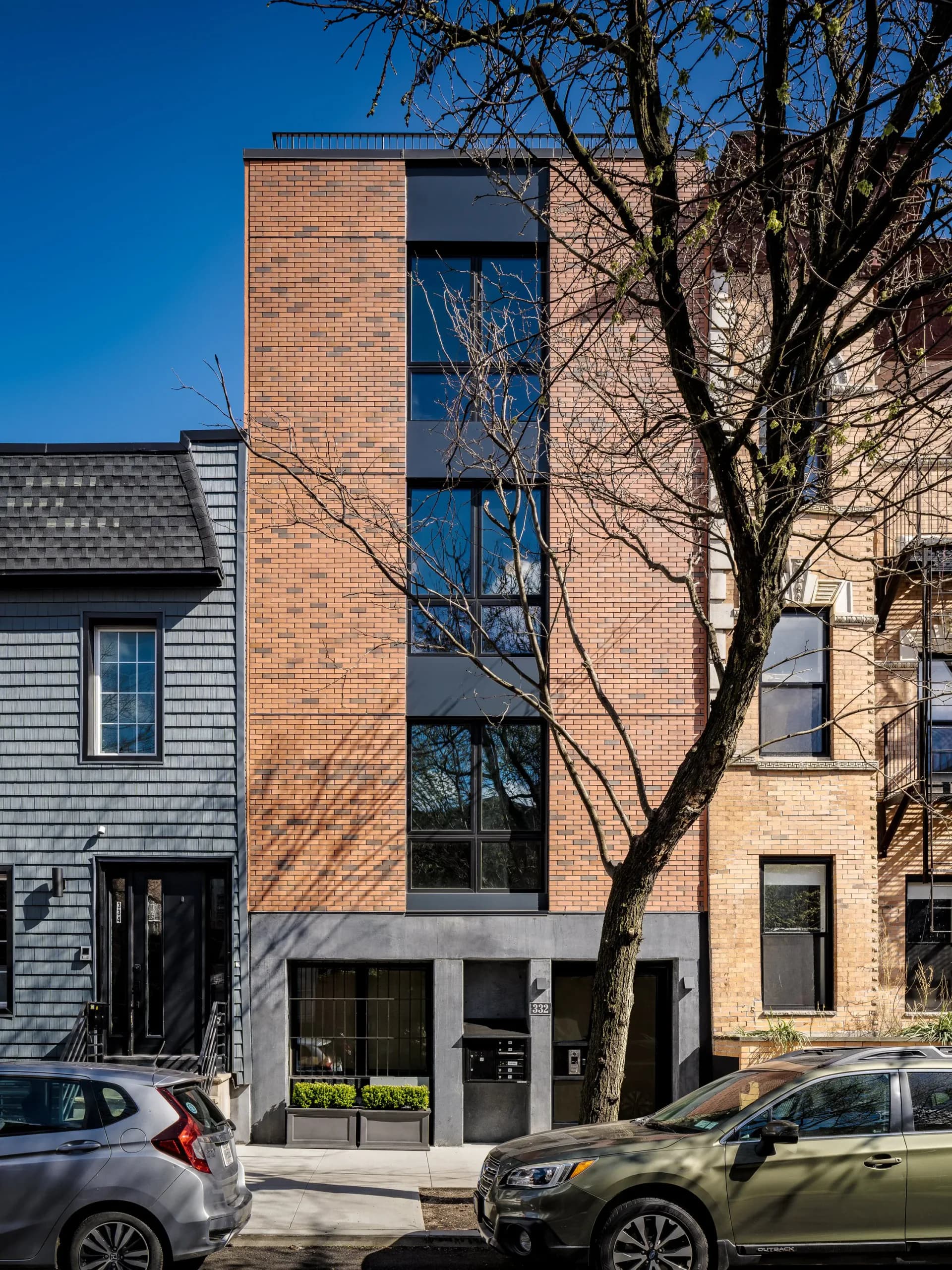 Narrow brick townhouse with tall vertical window and dark ground-floor storefront, contemporary architecture by Suzanna Tharian.