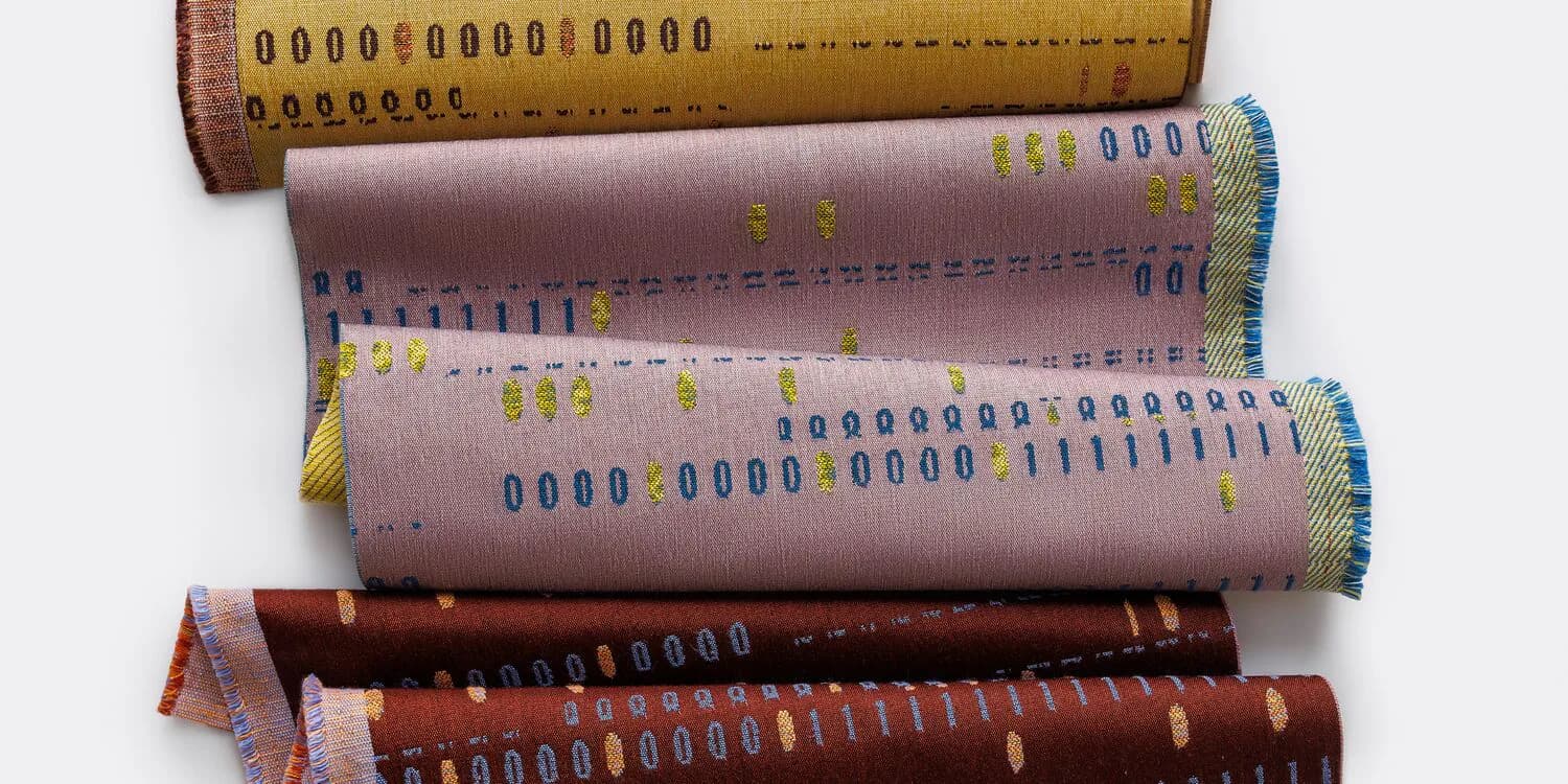 Rolled fabric samples displaying woven textile patterns in earth tones and blues, showcasing Suzanne Tick's material design work.