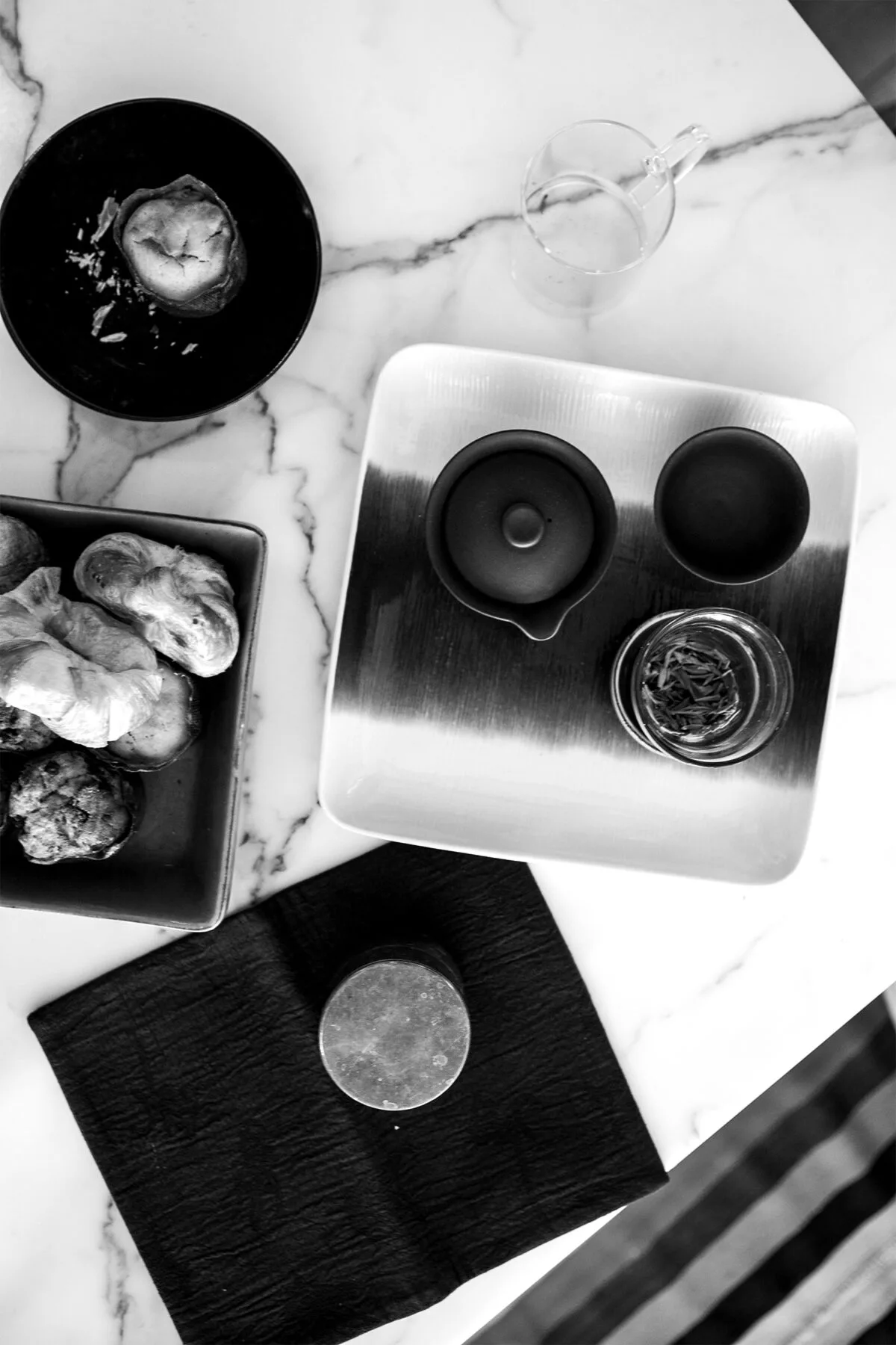 Monochromatic flat-lay food styling featuring plated dishes, glassware, and utensils arranged on marble surfaces by Tammy Chou.