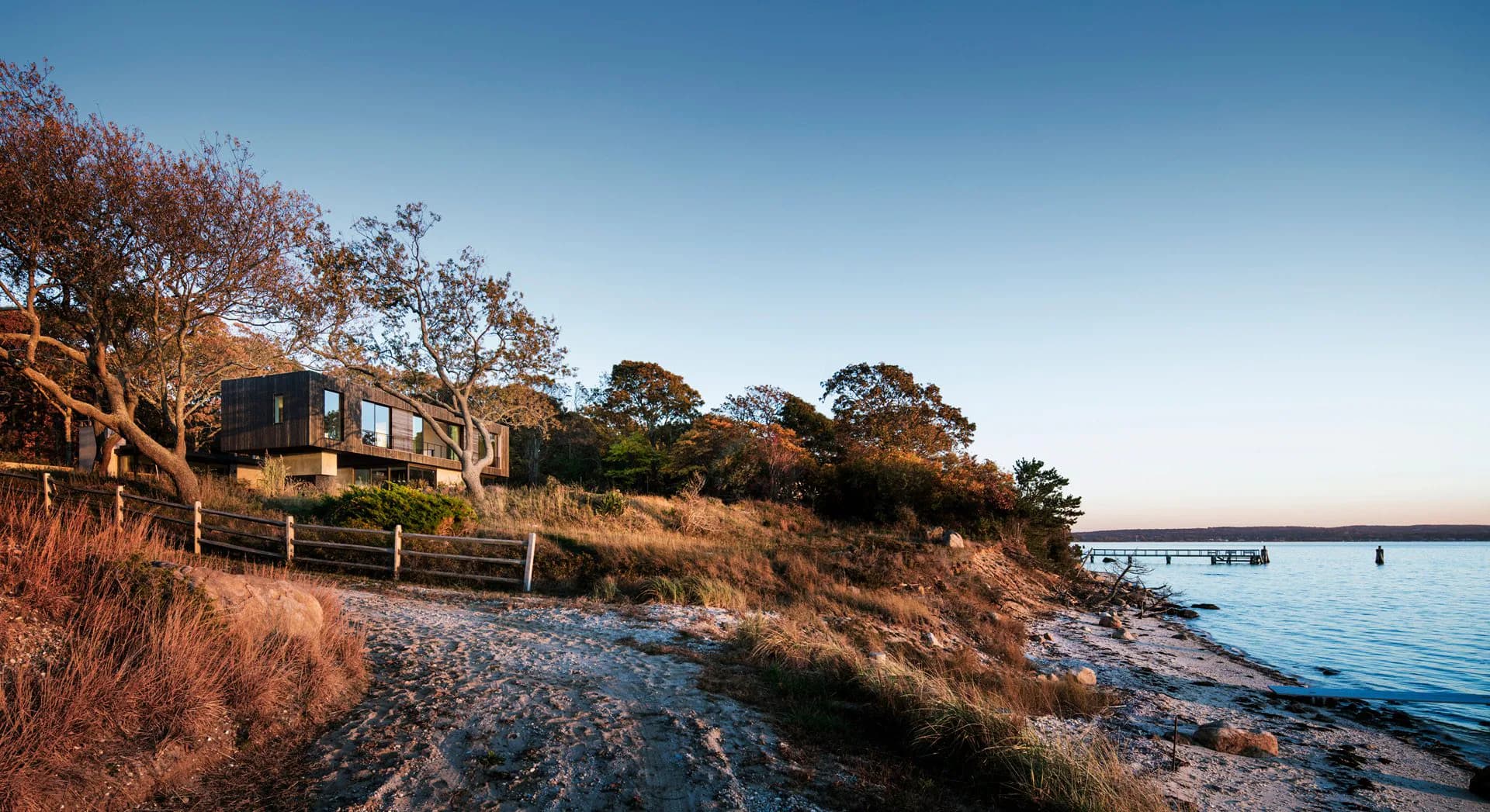 Modern residential structure nestled on a rocky coastal hillside with native vegetation and water views, designed by Tammy Mata-Lasky.
