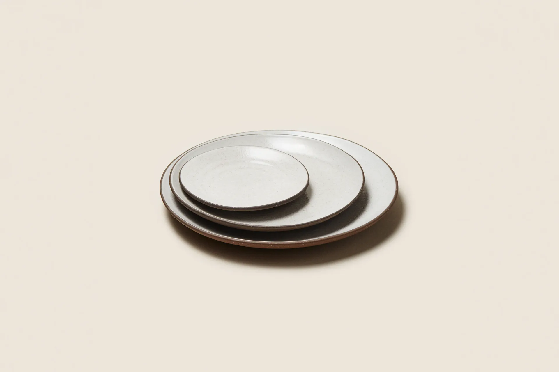 Nested white ceramic plates with dark rim detailing arranged in graduated sizes, showcasing minimalist tableware design by Tania Whalen.