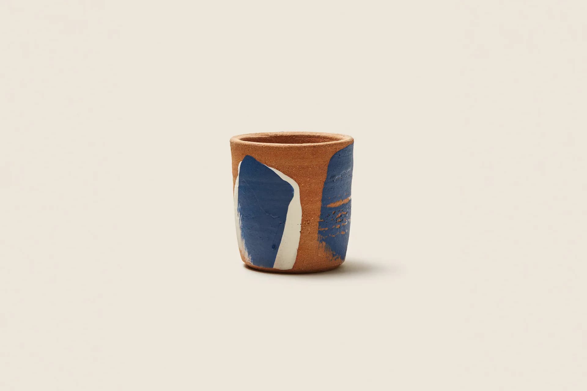 Handcrafted ceramic vessel with warm terracotta body and bold blue geometric panels, photographed against neutral background by Tania Whalen.