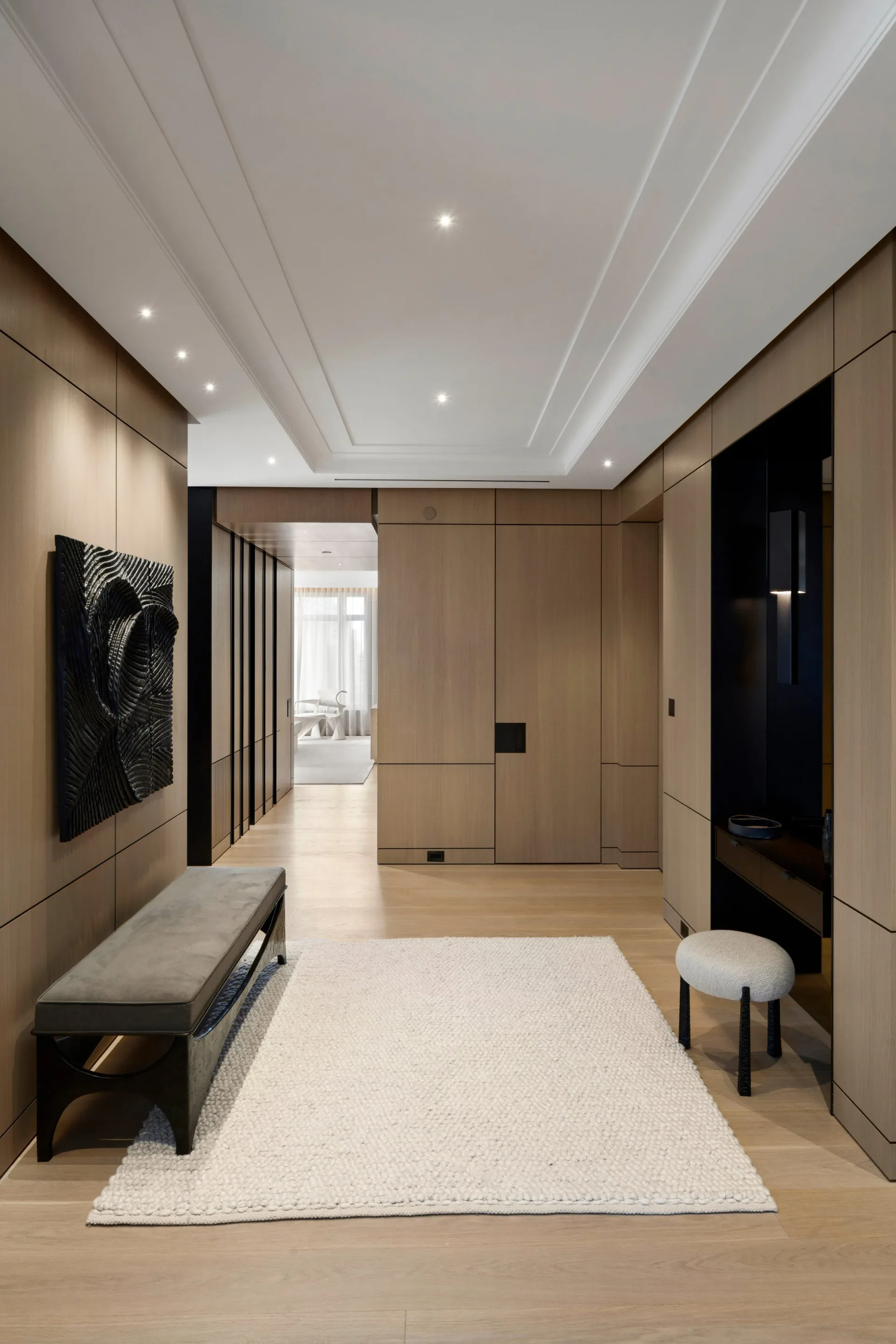 Modern entryway with taupe wall paneling, white coffered ceiling with recessed lighting, light wood flooring, and a cream area rug, designed by Tanishkaa Kumar.