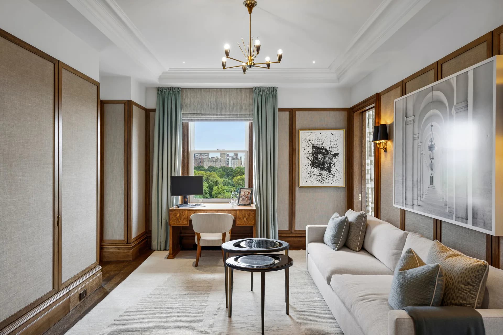 Luxurious hotel suite with warm wood paneling, cream upholstered seating, marble accents, and city views through large windows, designed by Tanishkaa Kumar.