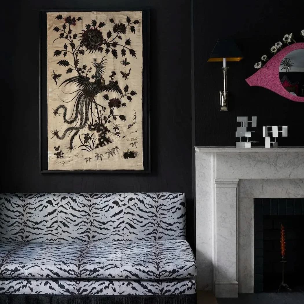 Black-walled interior featuring a zebra-patterned sofa, fireplace with sculptural pink fish art, and surreal botanical illustration by Tara McCauley.