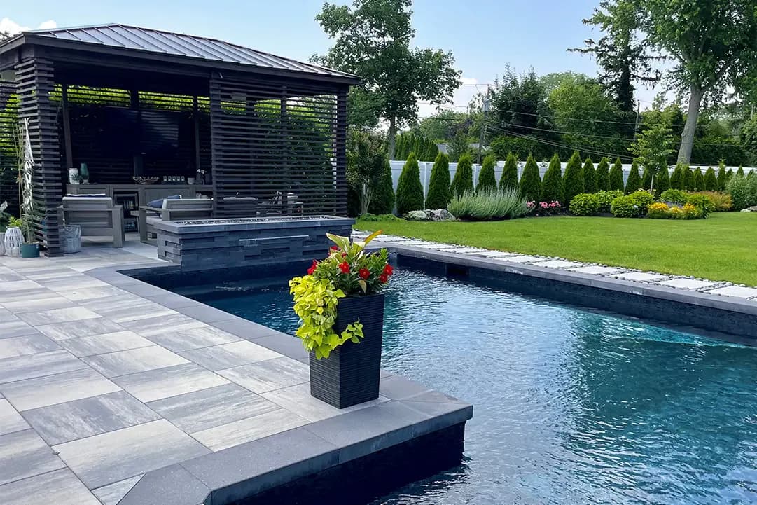 Contemporary poolside landscape with geometric paving, modern black pavilion, linear pool, manicured lawn, and planted borders by Tarena Cernuto.