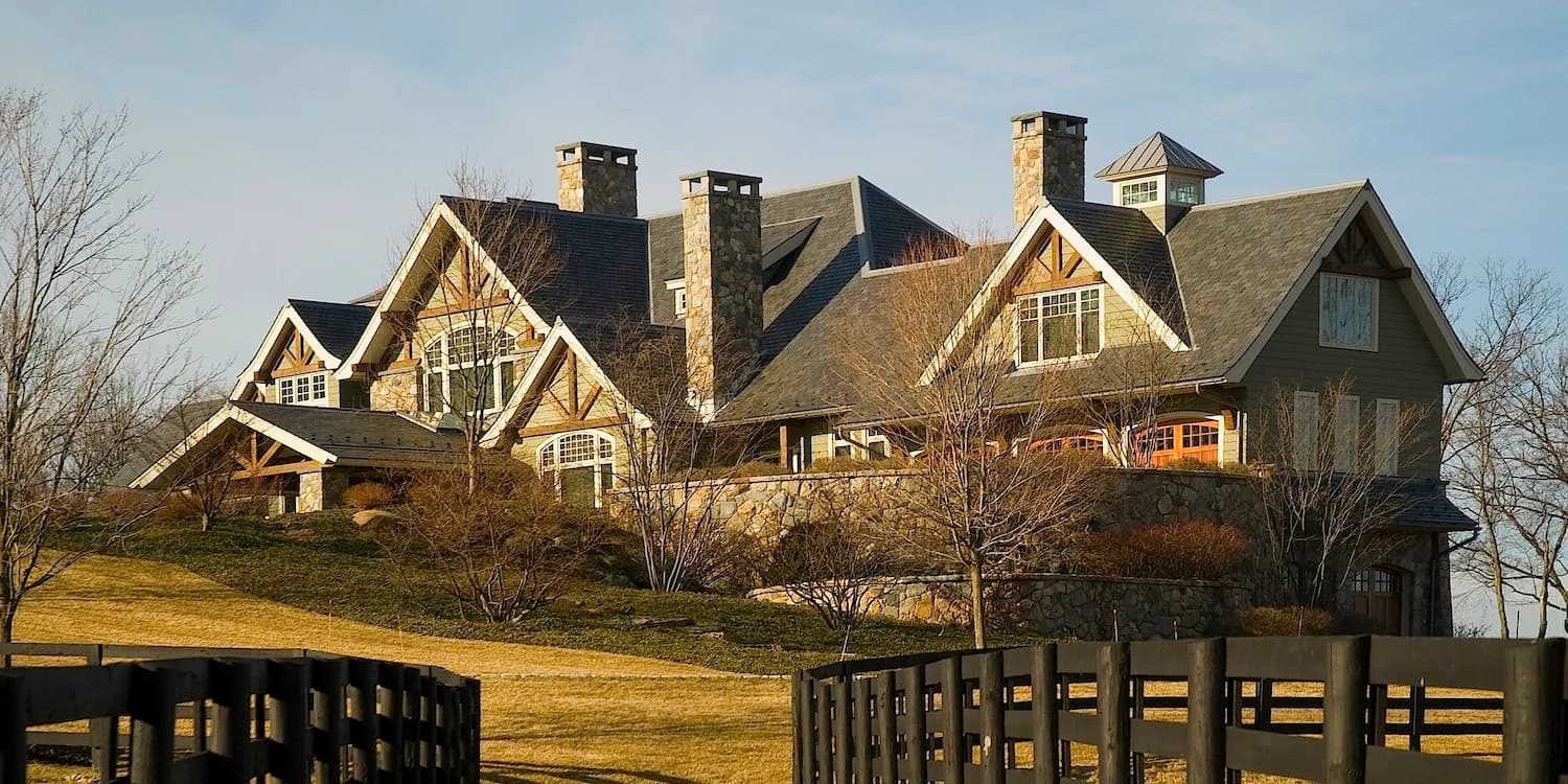 Large stone and timber residential estate with multiple gables, chimneys, and manicured grounds designed by Tasos Kokoris.