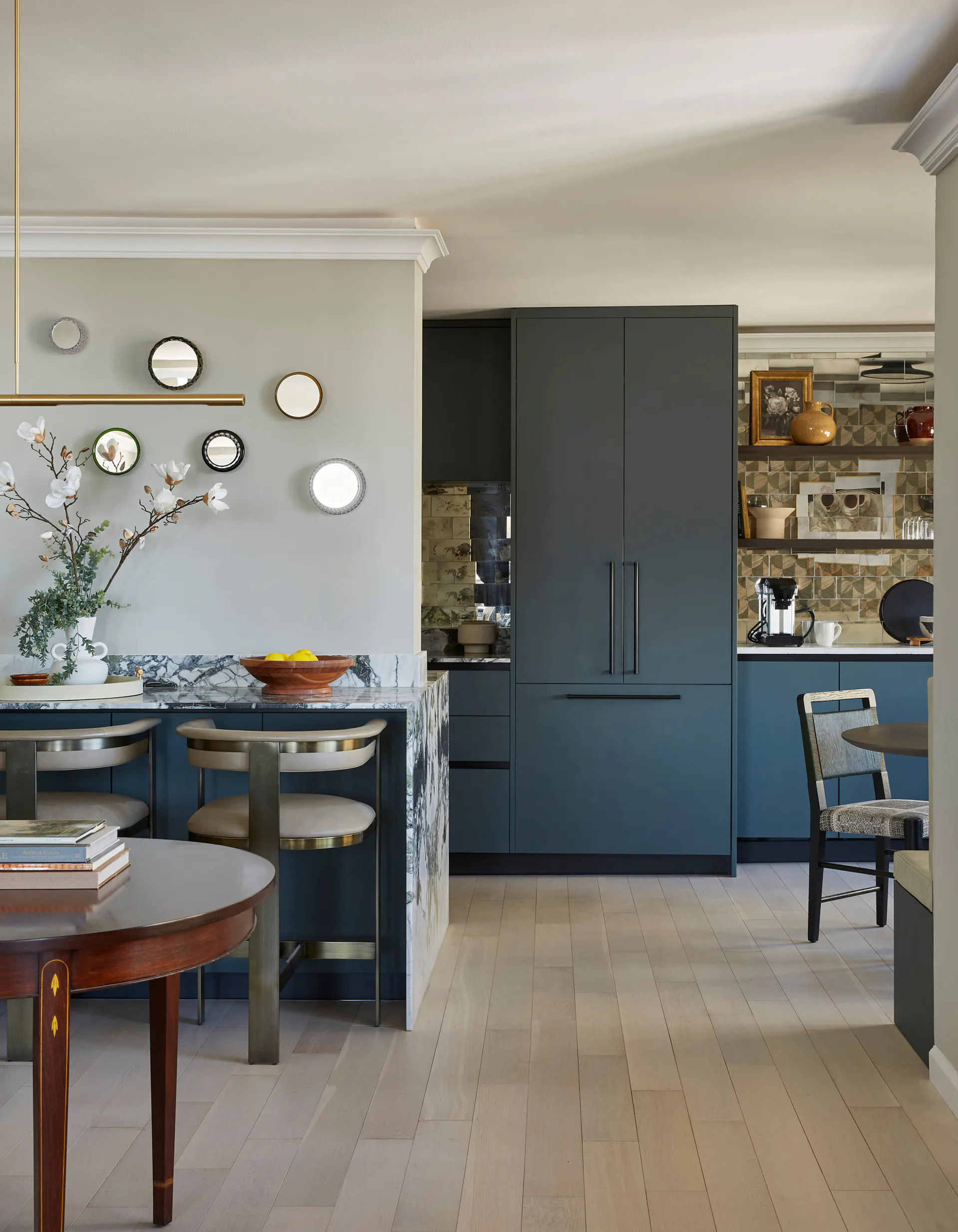 Contemporary kitchen and dining area with navy cabinetry, pale wood flooring, decorative plate wall, and mixed seating by Taylor Dieterich.