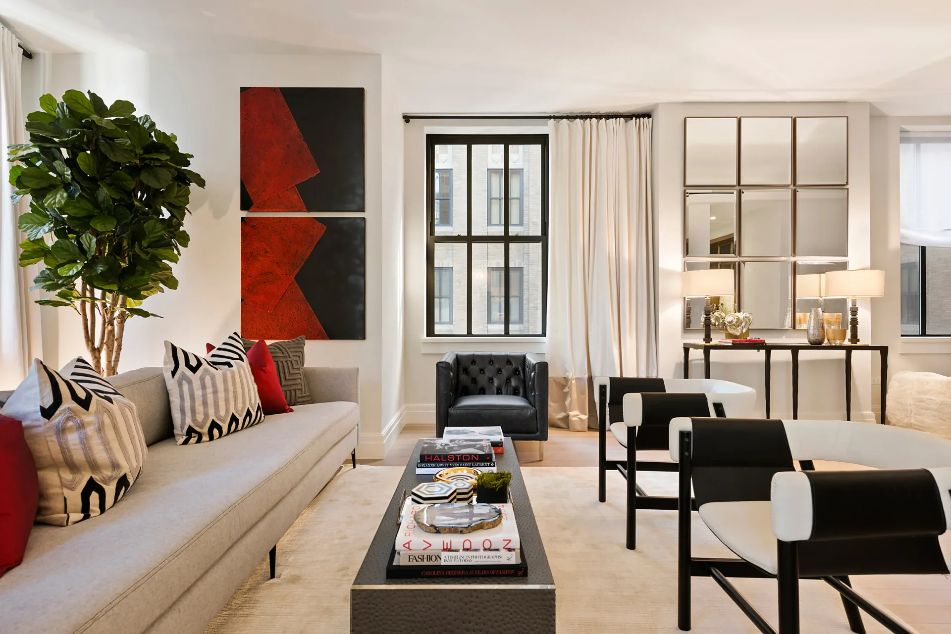Modern living room with cream sofa, black leather chairs, red abstract art, and black-framed glass doors overlooking a fireplace by Taylor Spellman.