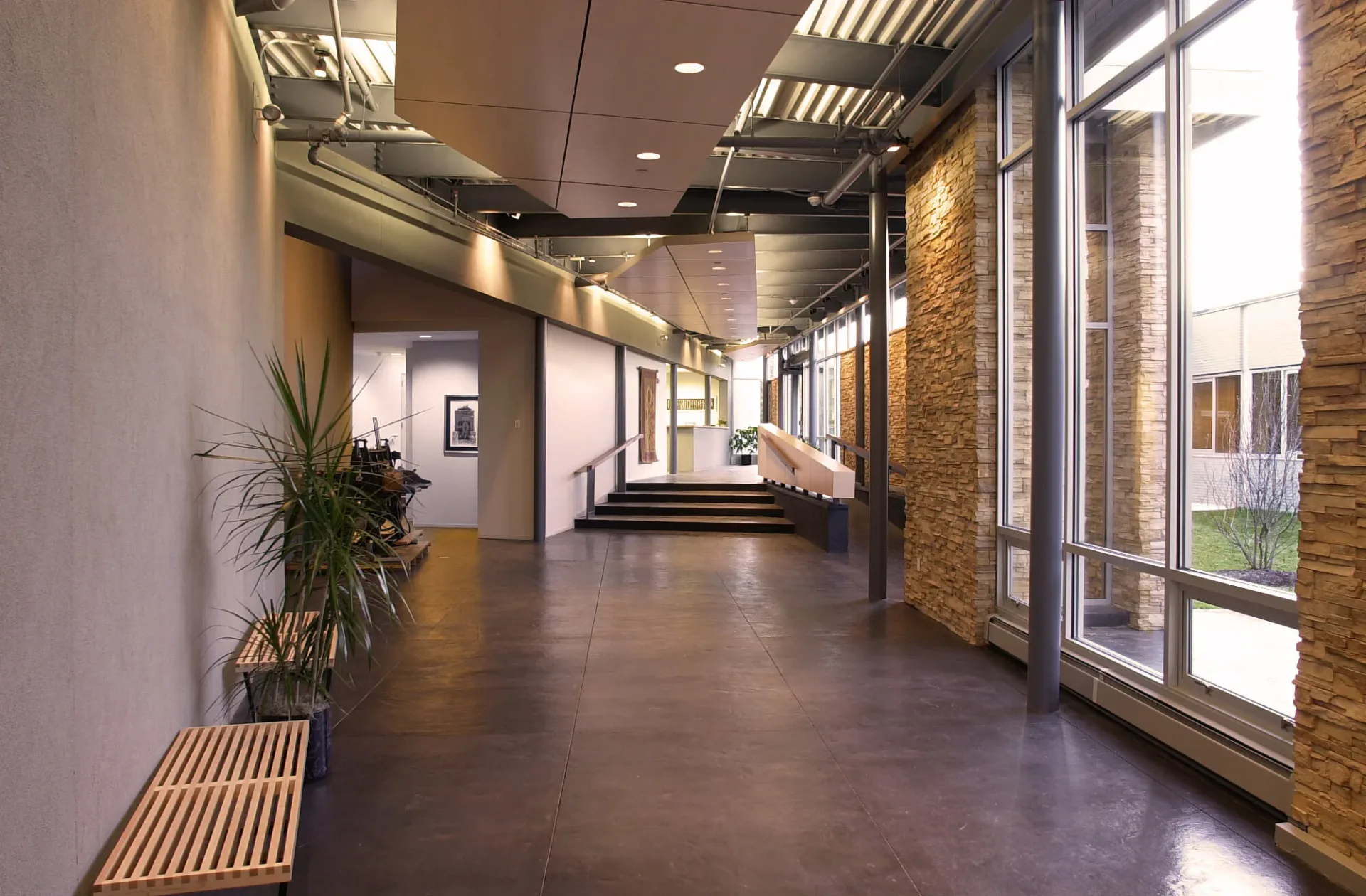 Modern corridor with exposed brick walls, polished concrete floors, linear ceiling lights, and floor-to-ceiling windows, designed by Terence Smith.
