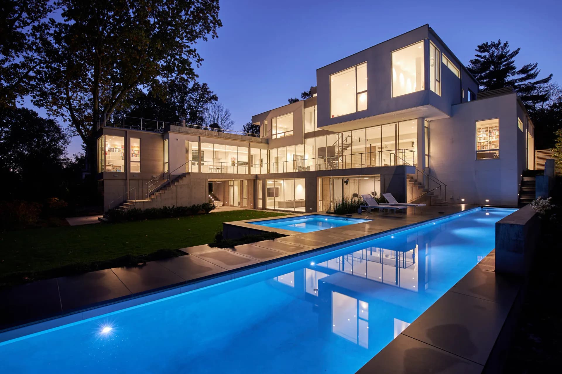 Modern residential house with illuminated interior and glowing swimming pool at dusk, designed by Terence Smith.