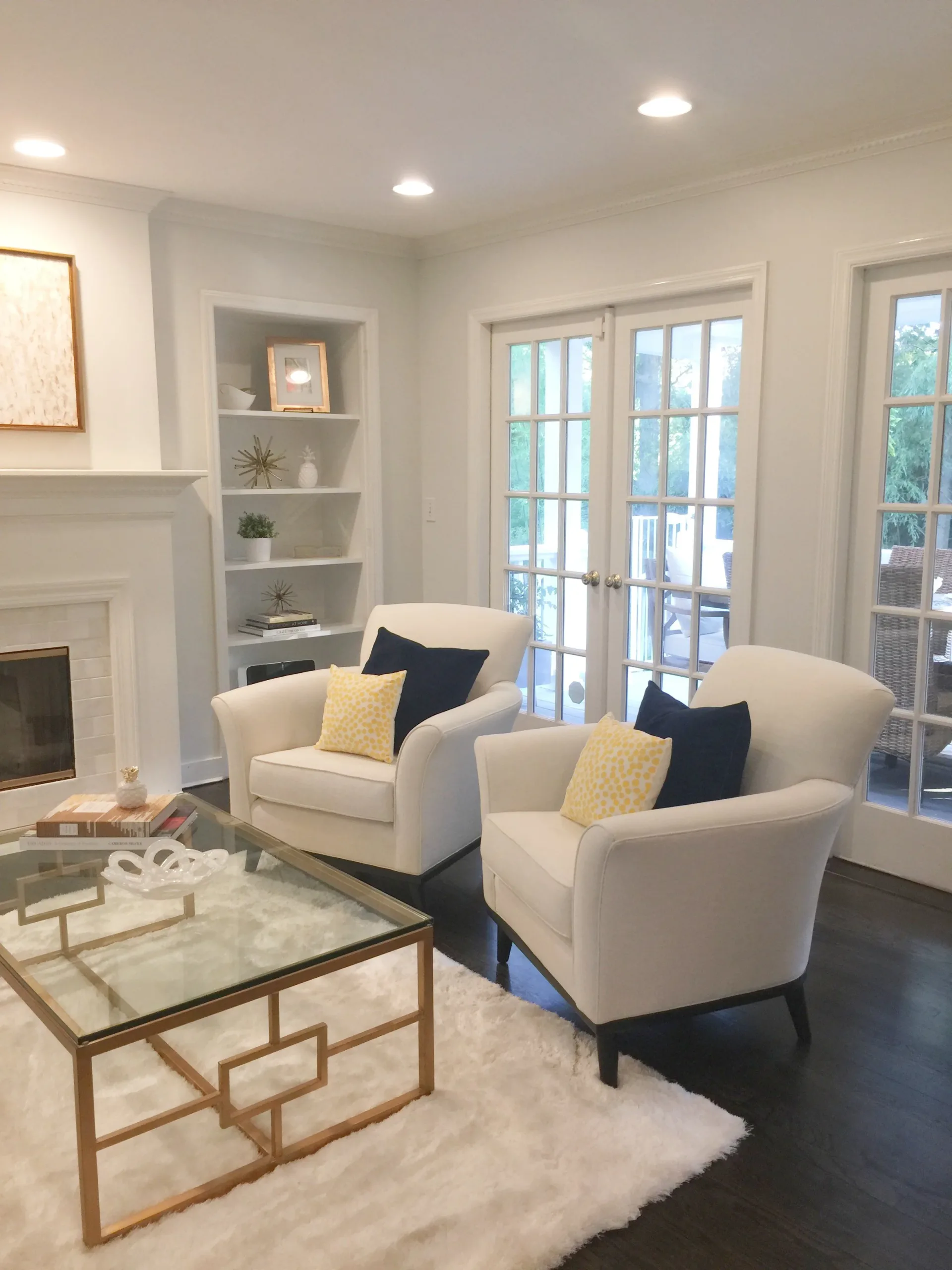 Modern living room with cream armchairs, fireplace, built-in shelving, and French doors opening to a terrace, designed by Terry Sachs.