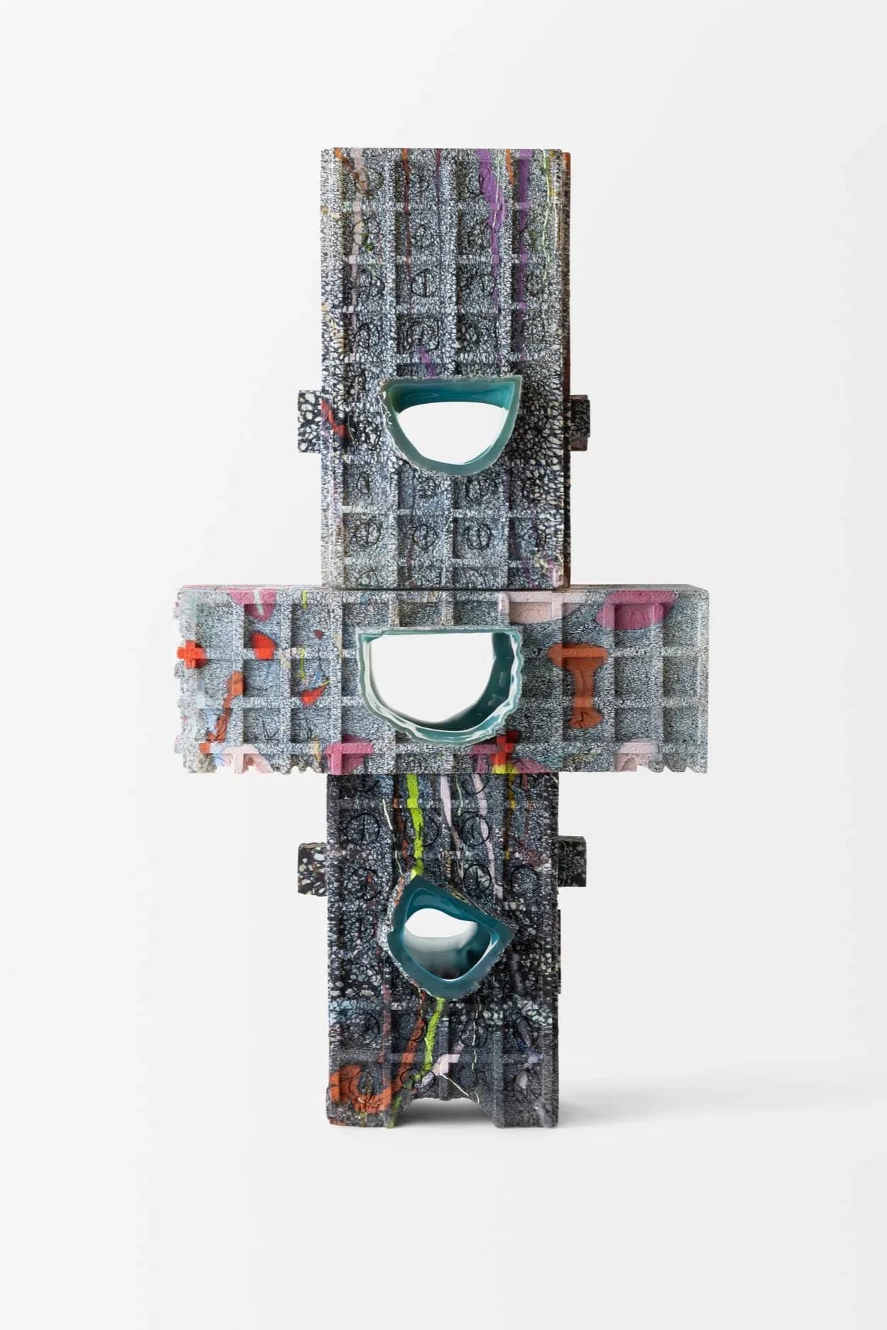 Stacked sculptural installation with three teal semi-circular cutouts through layered textile and material blocks, featuring colorful accents and text elements by Thaddeus Wolfe.