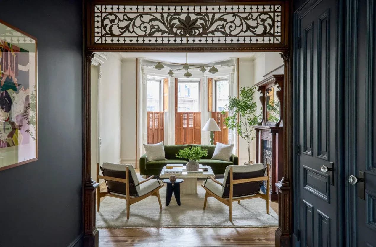 Elegant foyer with ornamental transom, dual mid-century modern chairs, round black table, and French doors opening to garden by Themis Haralabides.