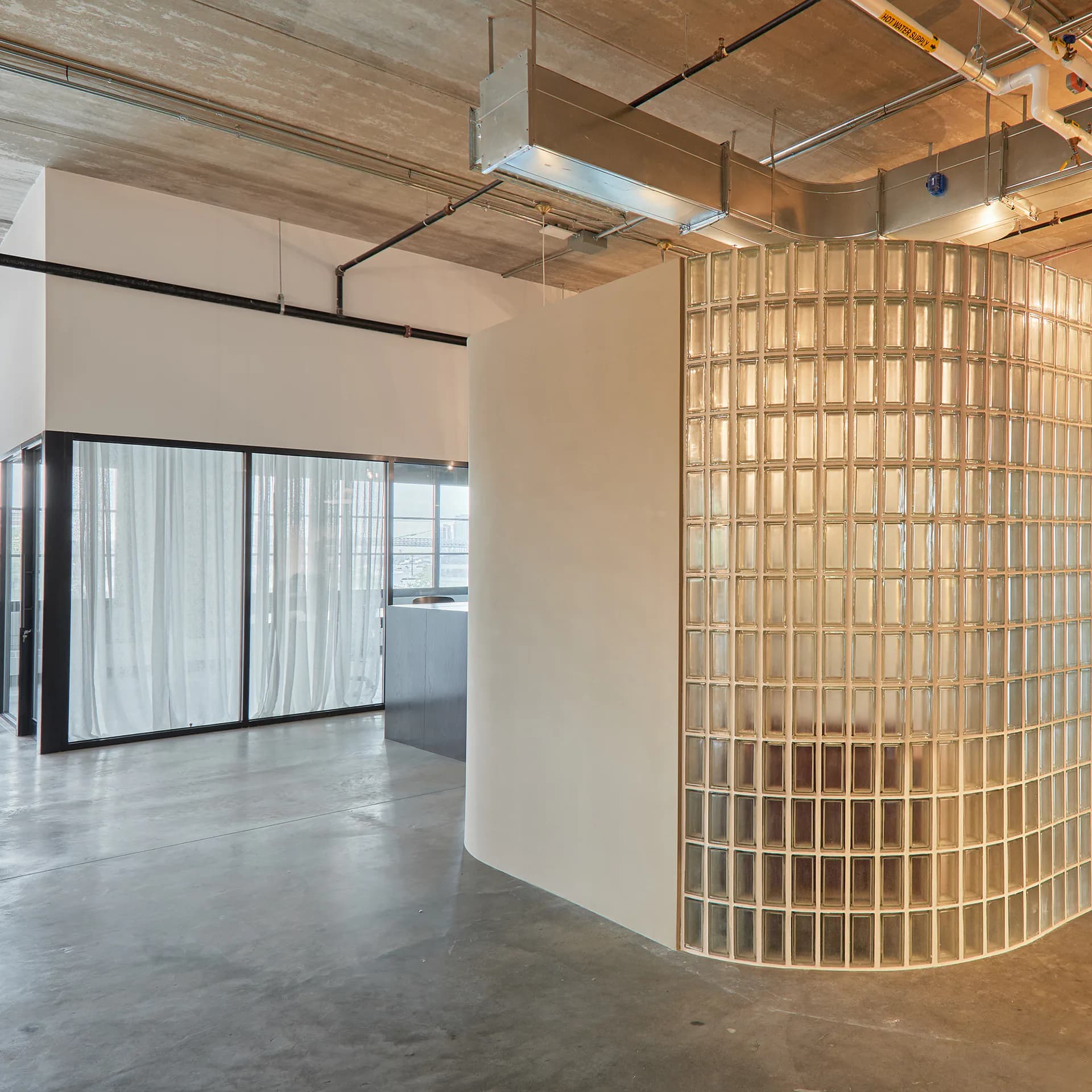 Industrial loft space featuring a curved wooden lattice partition and frosted glass room dividers with concrete flooring and exposed ceiling by Theo Guo.