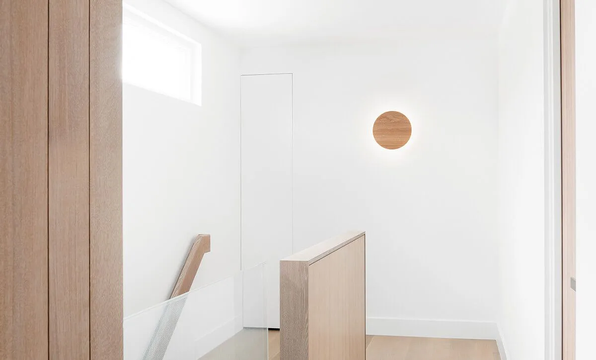 Minimalist interior stairwell with white walls, wooden handrail, and circular wooden accent on wall by Theo Richardson.